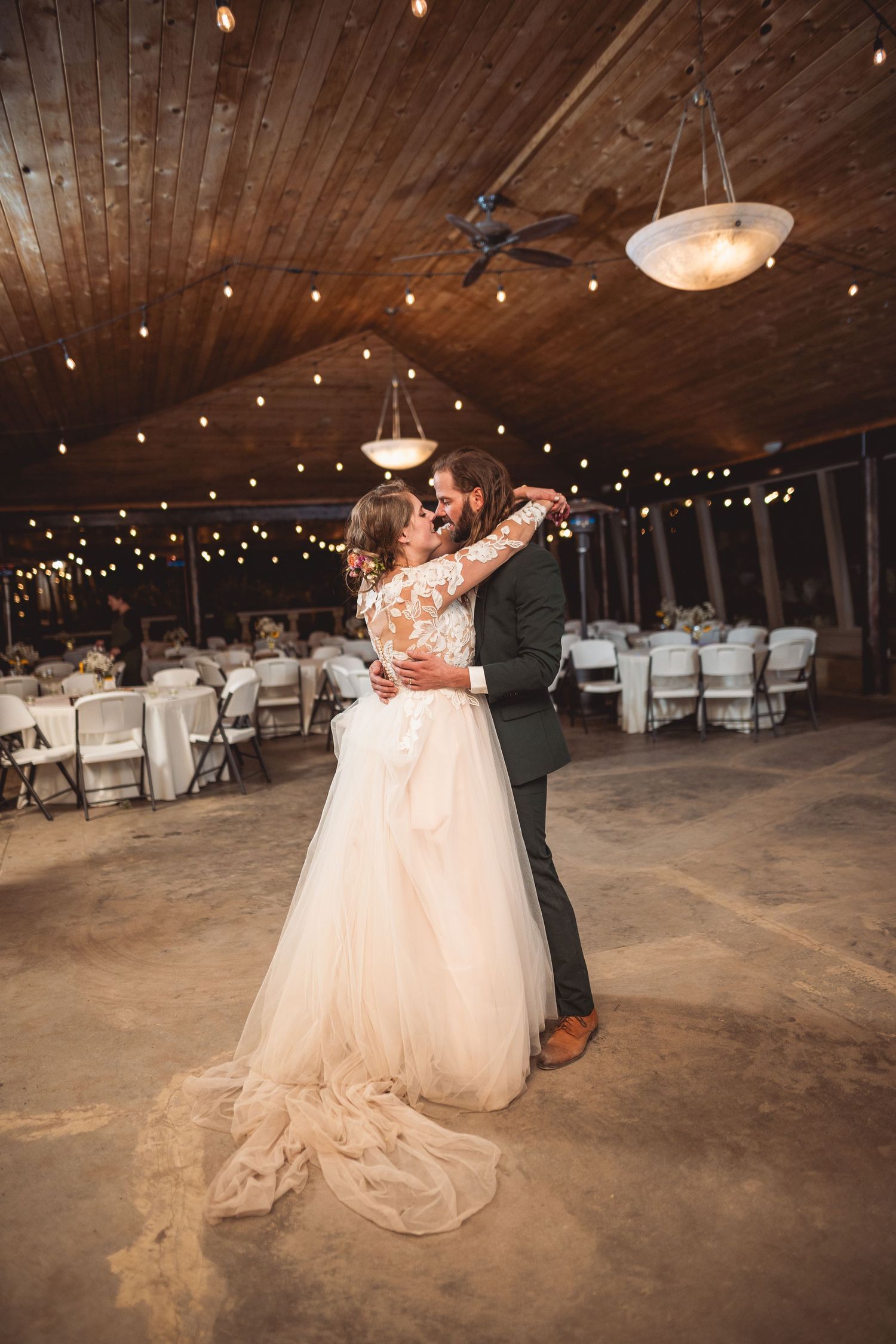 Dancing couple spins on rustic wooden floor under romantic string lights.