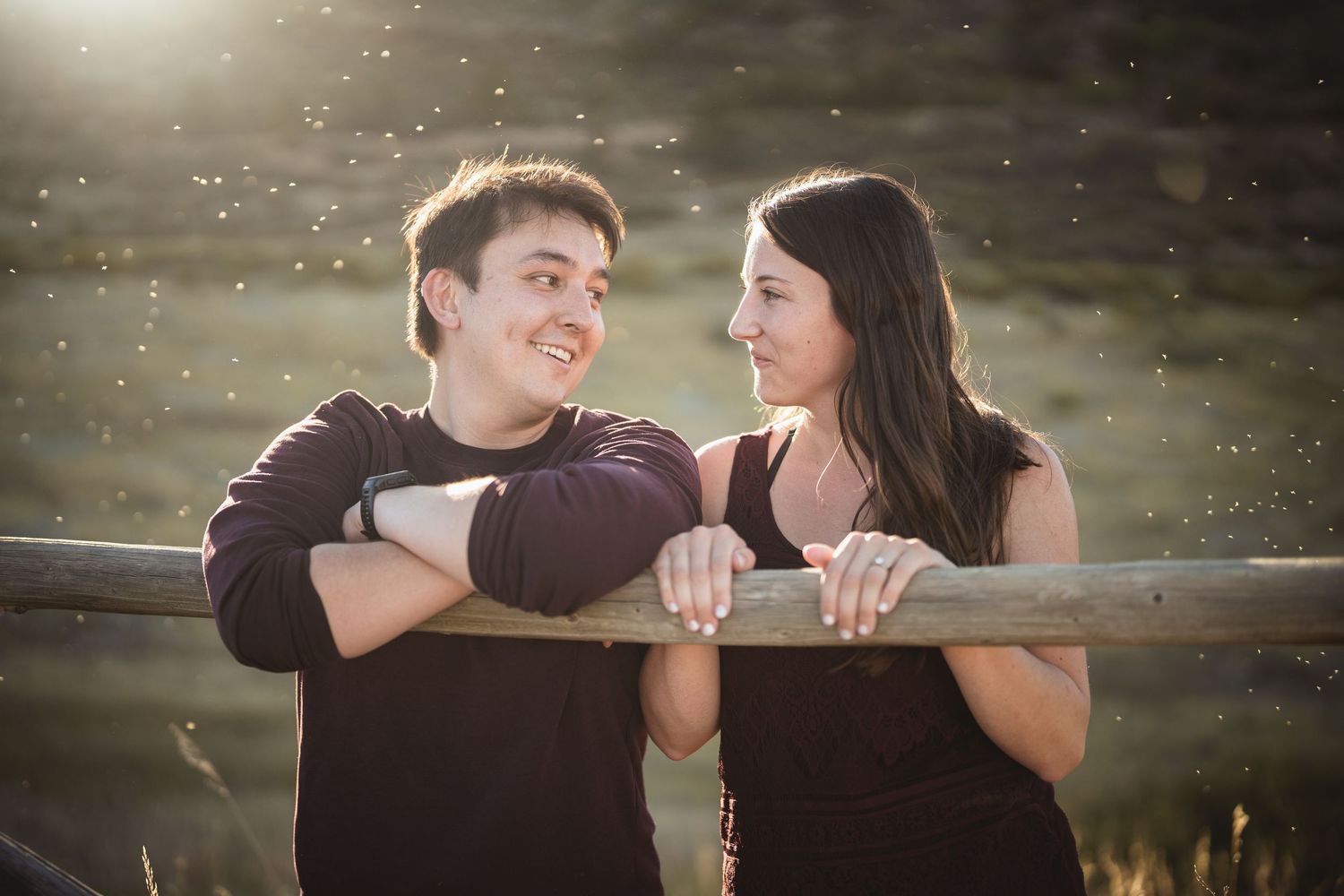 Romantic couple shares an intimate moment on a wooden fence at sunset.