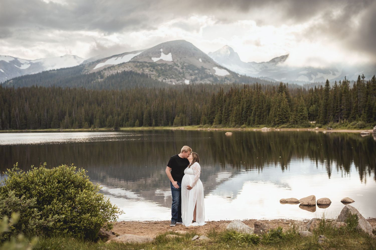 Two silhouettes share an intimate moment against a mountain lake backdrop.