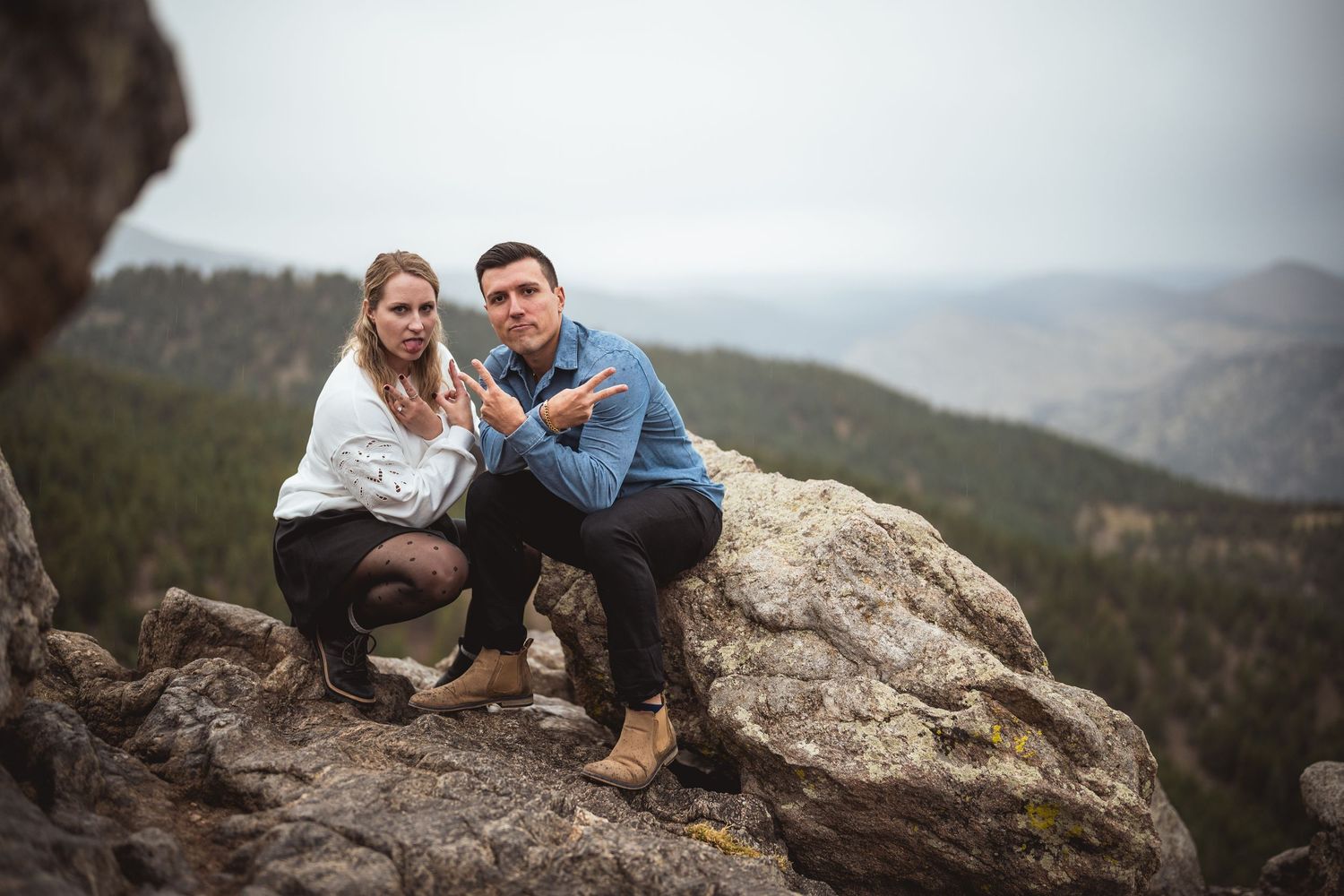 Couple posing on a rocky mountain summit with scenic forest valley views in the background.