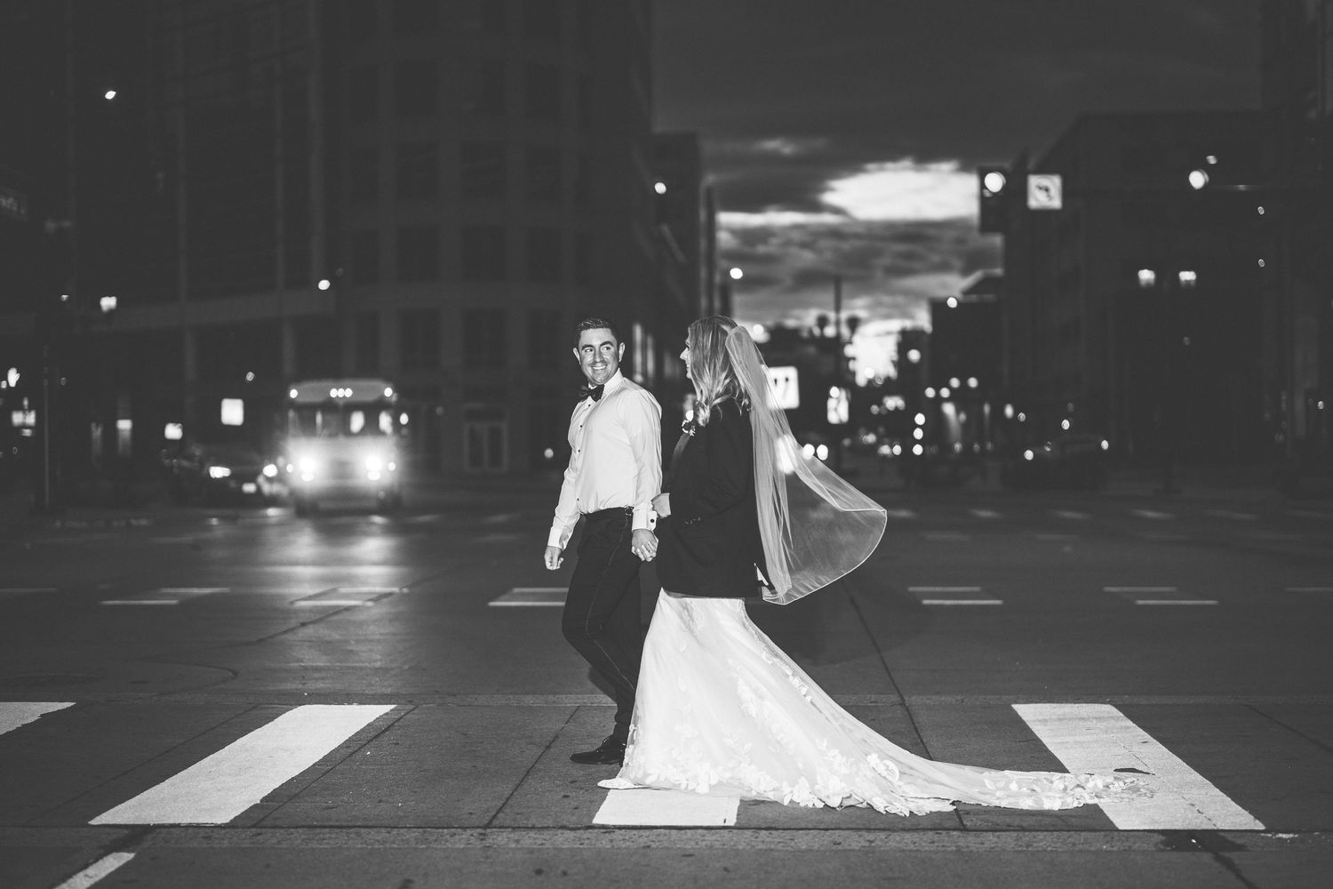 Dramatic nighttime wedding photos illuminated by city lights in an urban setting.