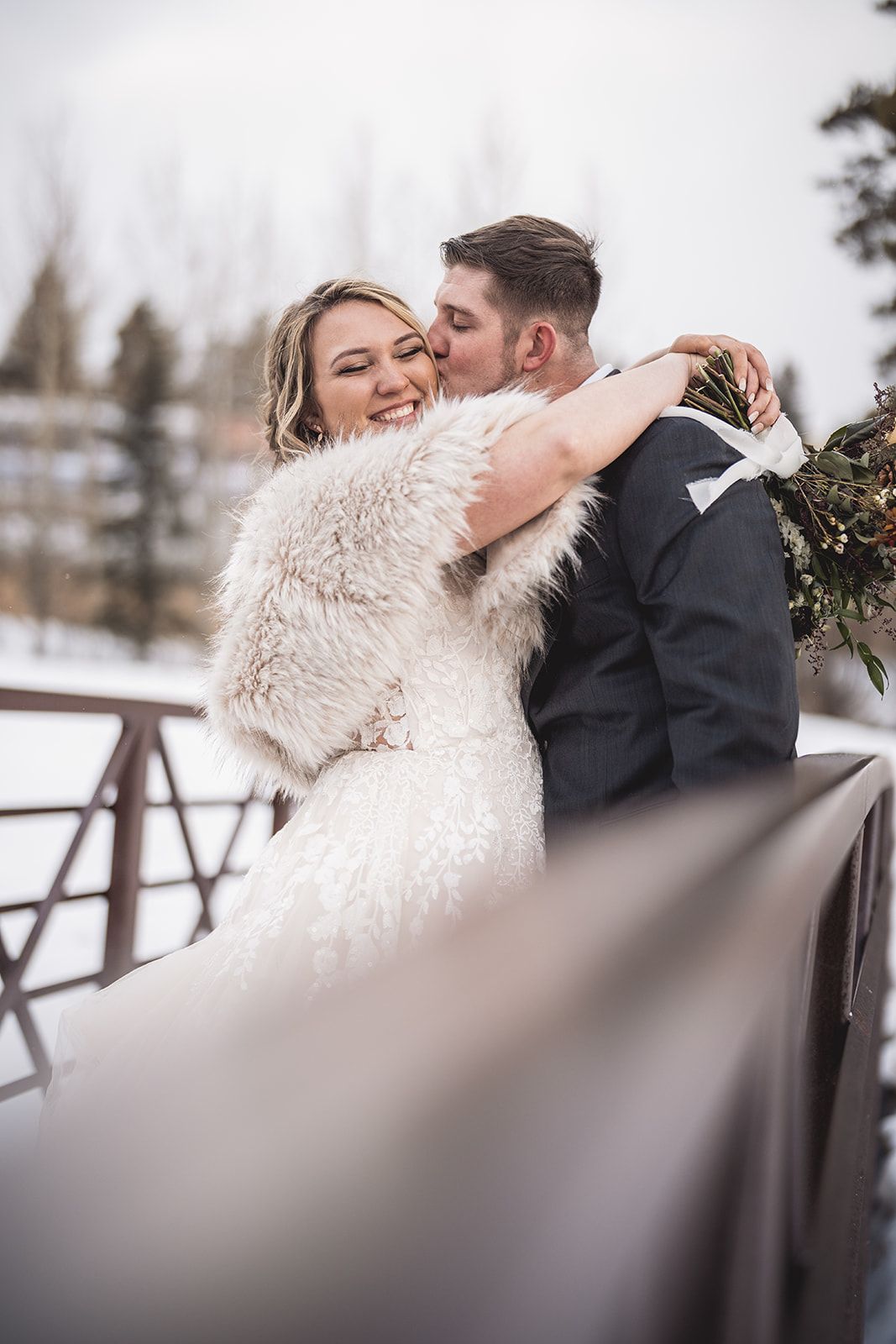 A romantic winter wedding scene with a couple embracing in the snow wearing a white dress and dark suit.