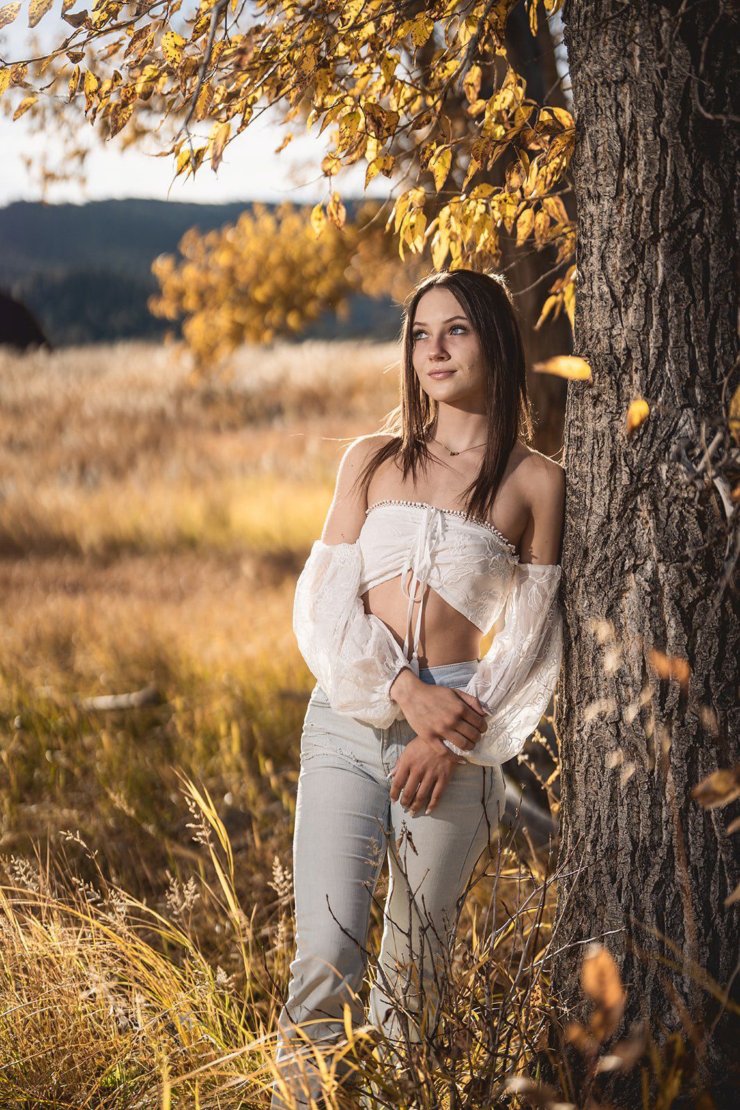 A white lace top outfit styled with autumn leaves framing the rustic outdoor portrait setting.