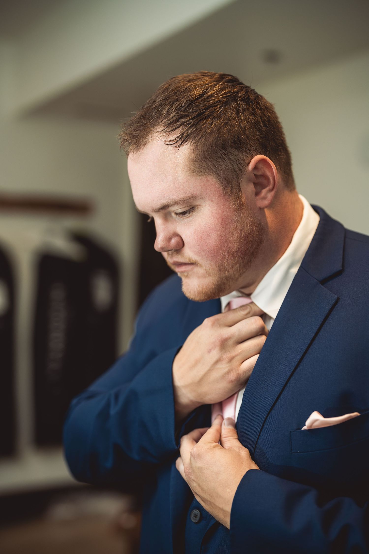 Person in navy suit and pink tie adjusting collar.