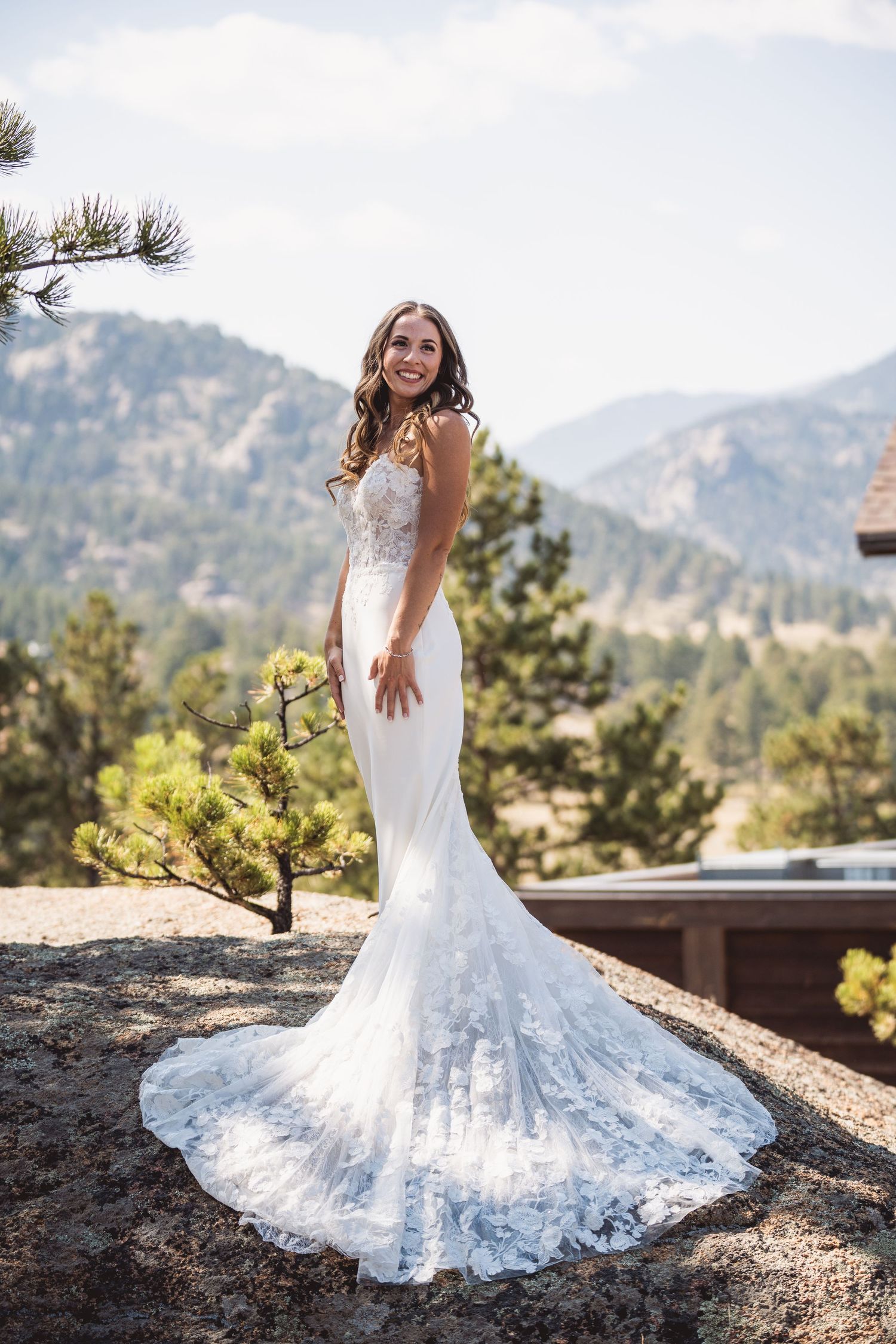 A white lace wedding dress flows elegantly against a mountain landscape backdrop.