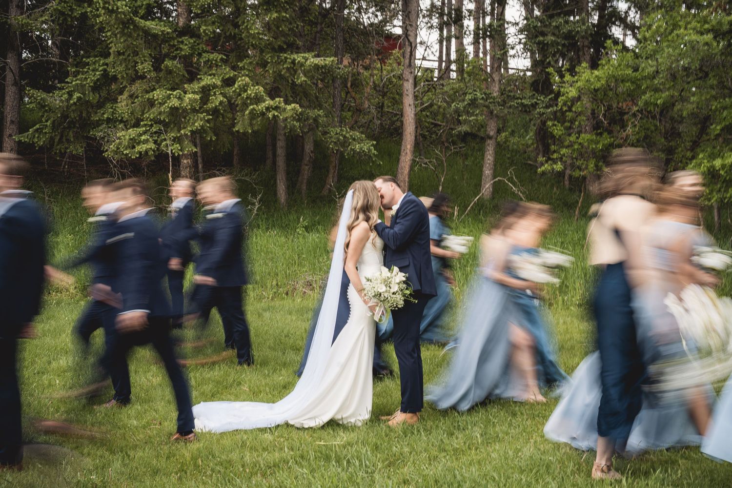 Wedding party running together through forest clearing in coordinated blue attire.