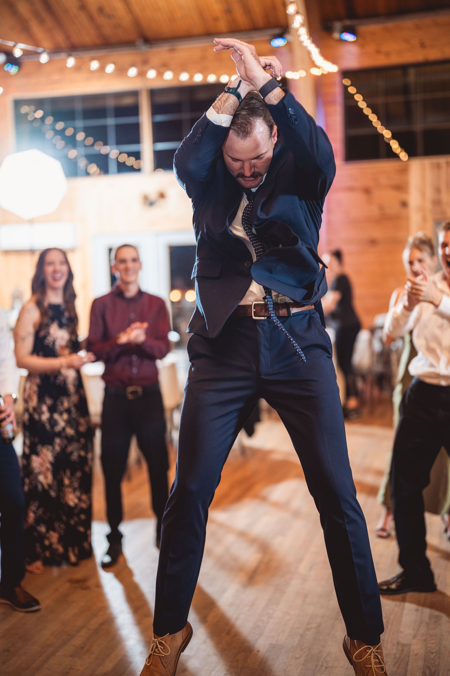 Dancing guests on a wooden floor at a wedding reception with string lights overhead.