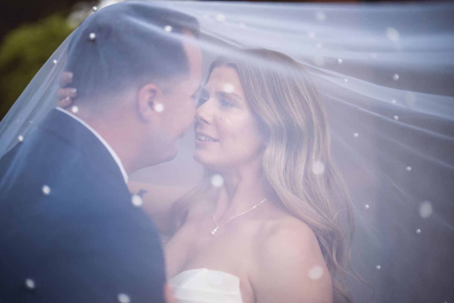 Intimate moment captured under flowing wedding veil with sparkling details.