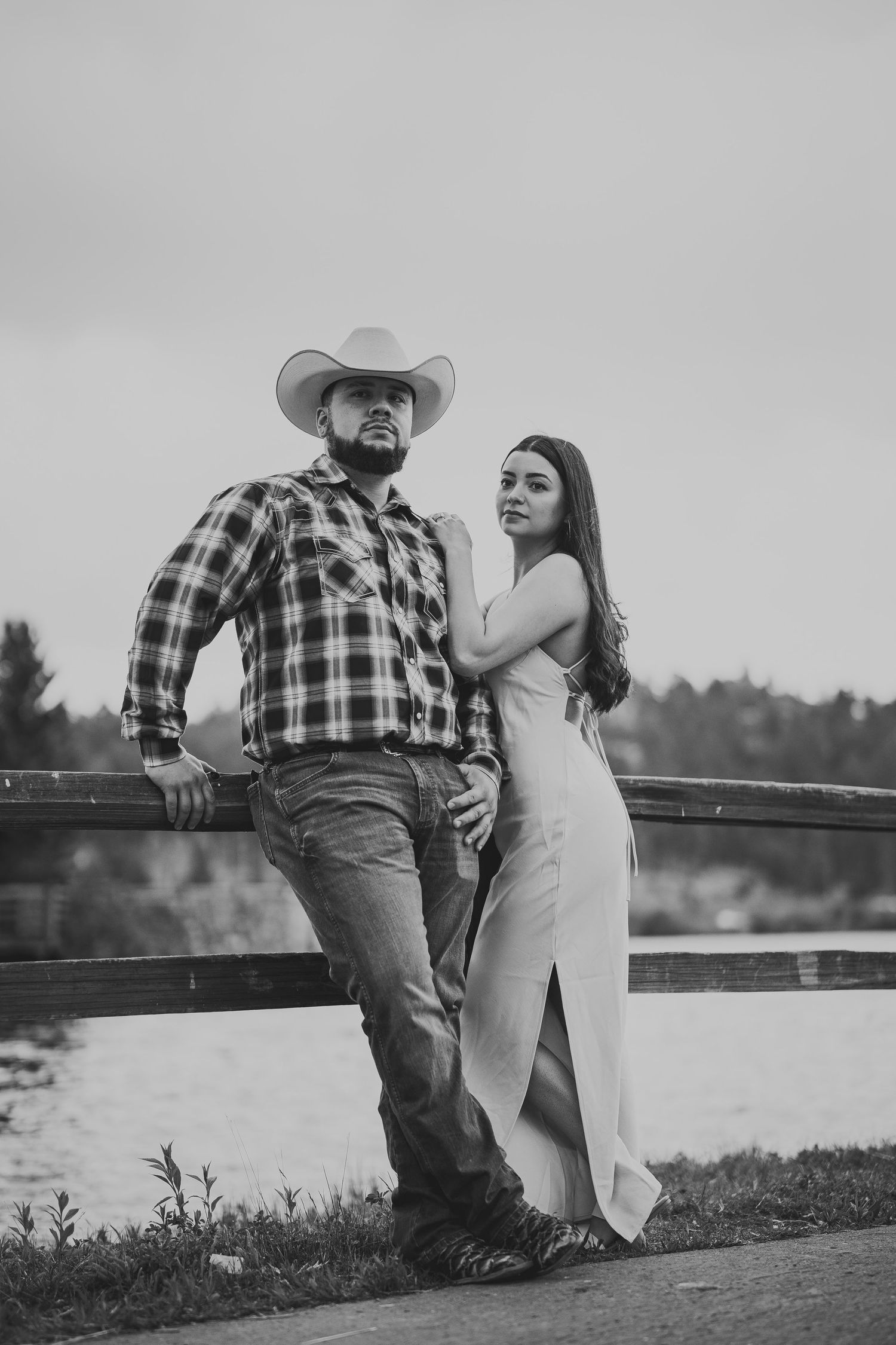 Romantic black and white scene of a couple sitting on a wooden fence by a lake.