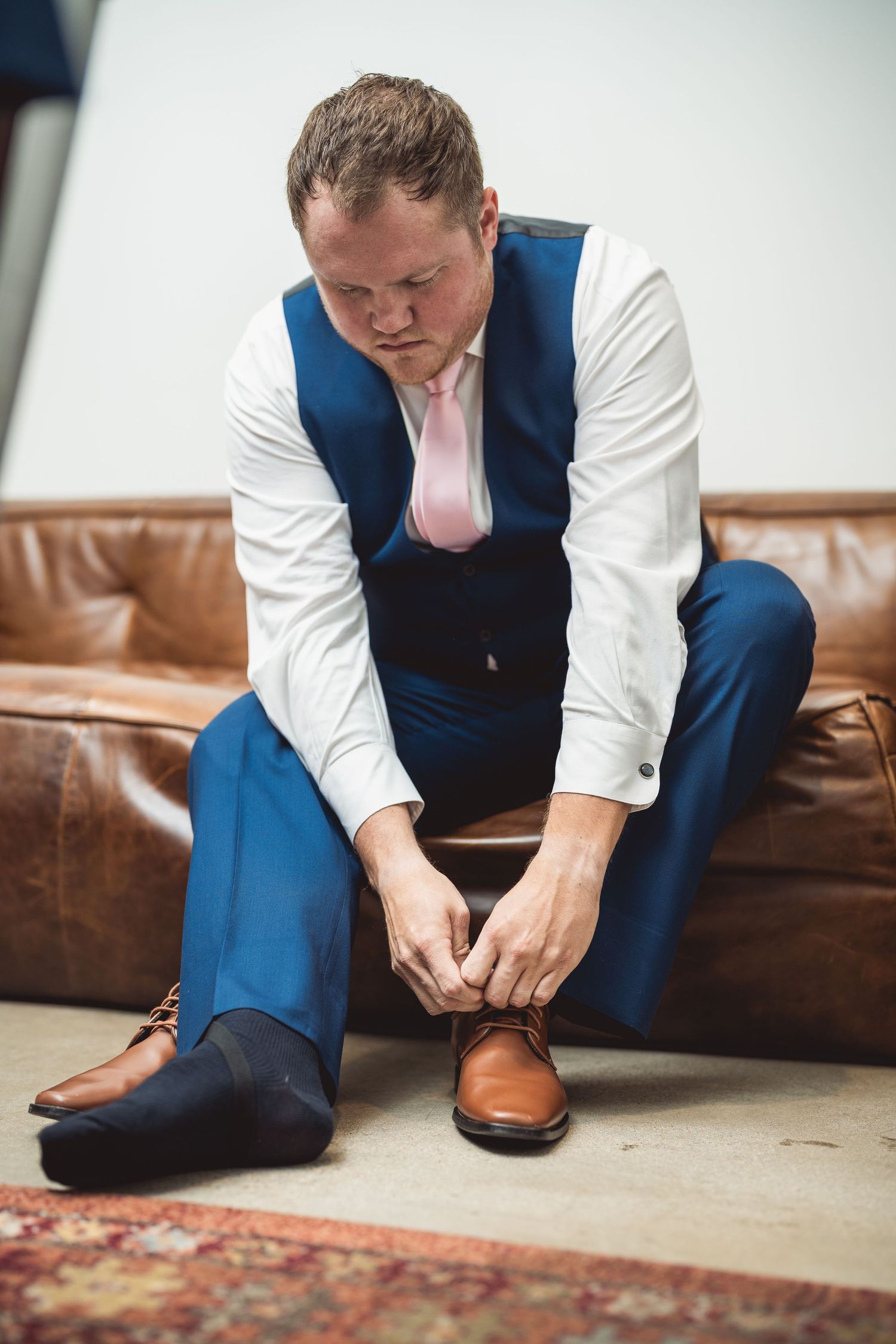 Close up of groom adjusting brown leather dress shoes before wedding ceremony.