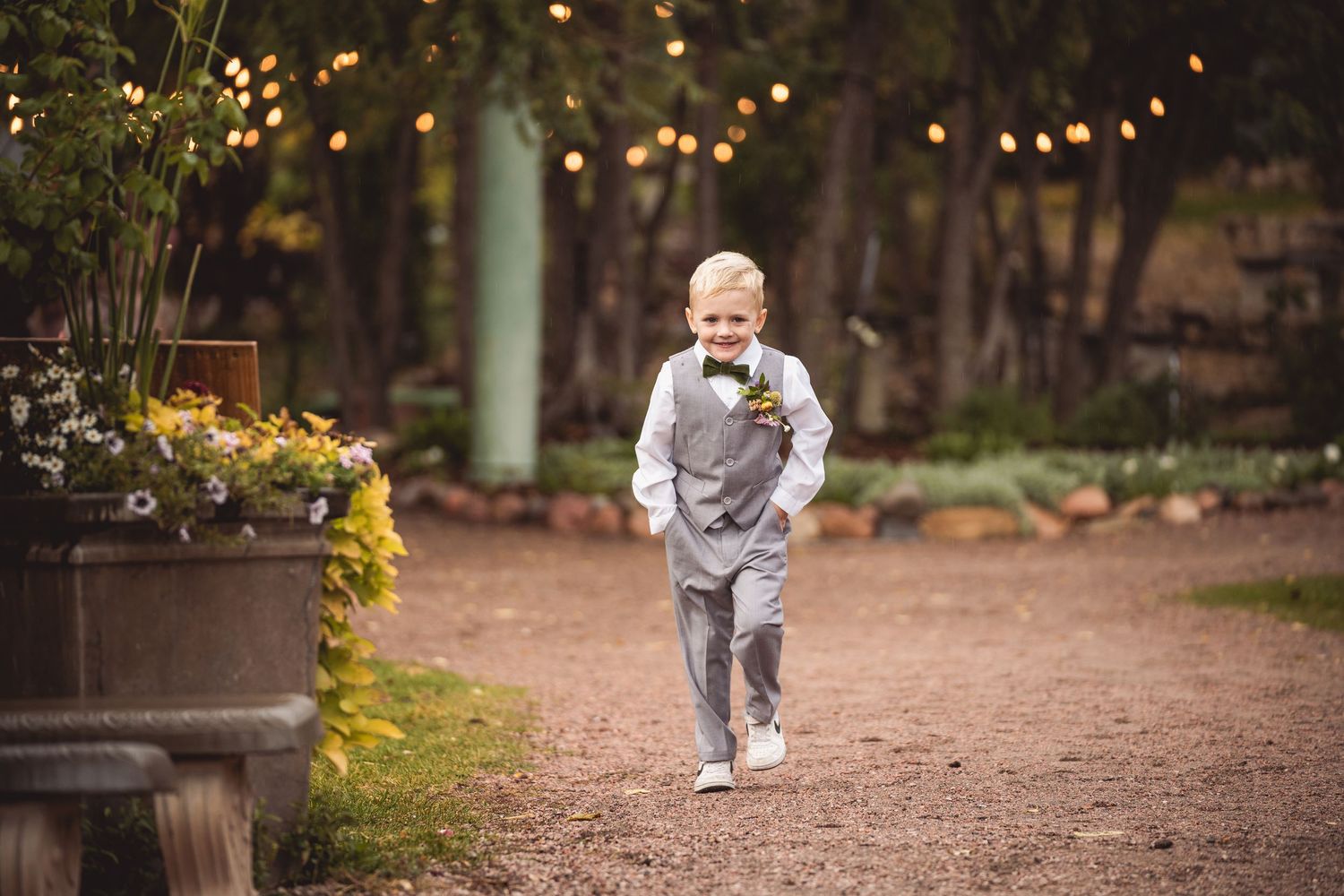 Child in formal attire running along illuminated garden path at dusk.