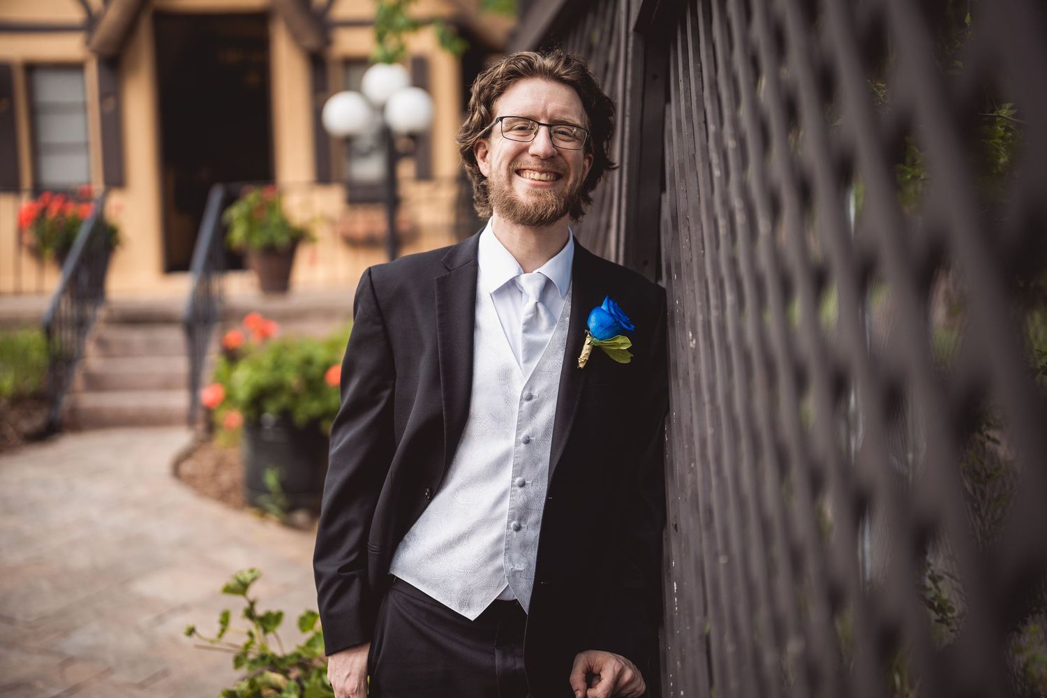 A cheerful groom with a blue boutonniere poses against a textured black wall.
