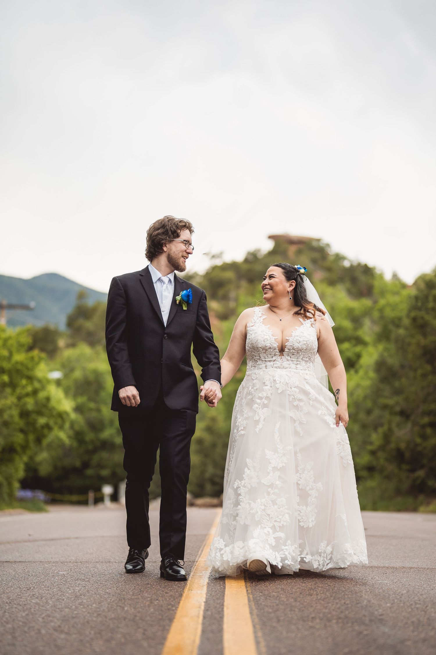 A couple shares a joyful moment in their wedding attire on an outdoor path surrounded by greenery.