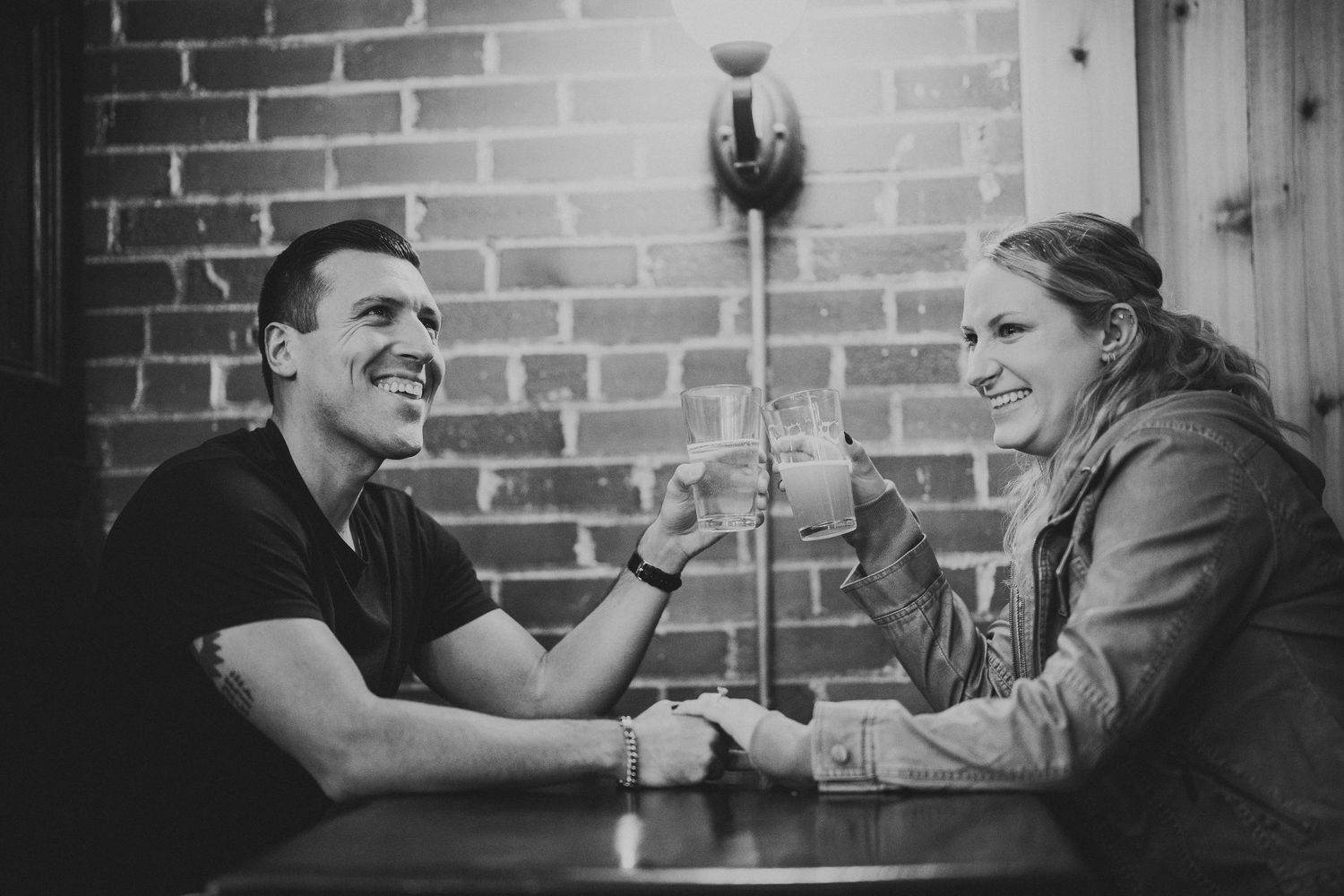 A couple shares drinks and conversation at a rustic brick-walled restaurant.