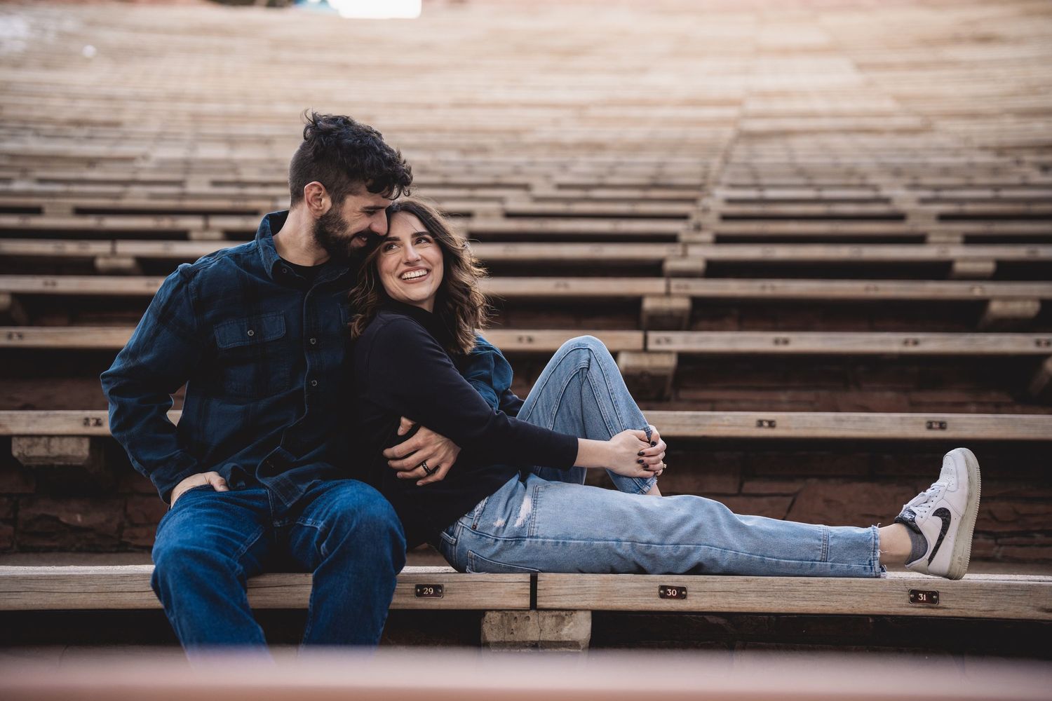 A couple relaxing on wooden stadium bleachers during a photoshoot.