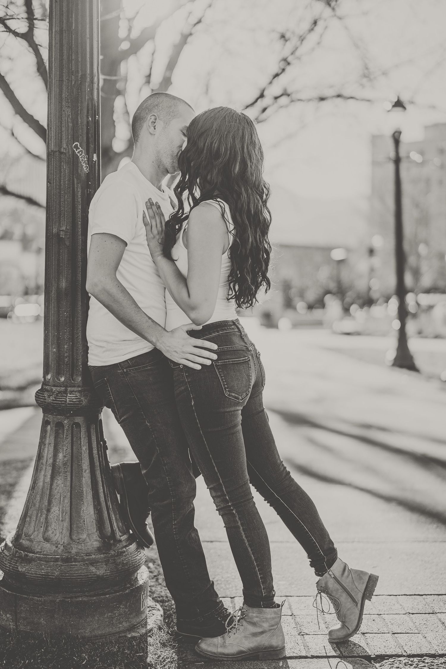 A romantic black and white photo of a couple embracing by a vintage street lamp.