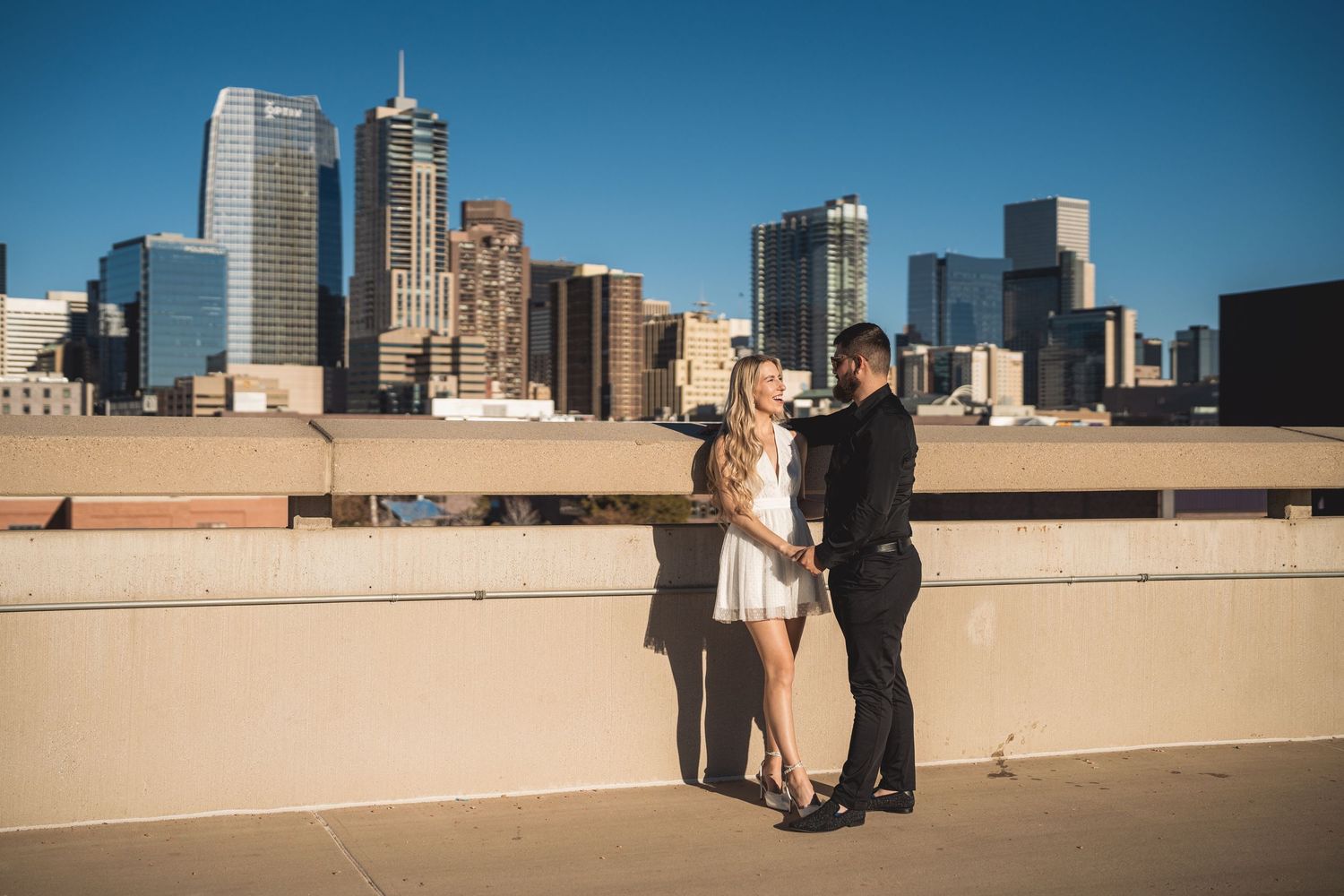 Couple sharing a romantic moment on a rooftop with a stunning city skyline backdrop on a sunny day.