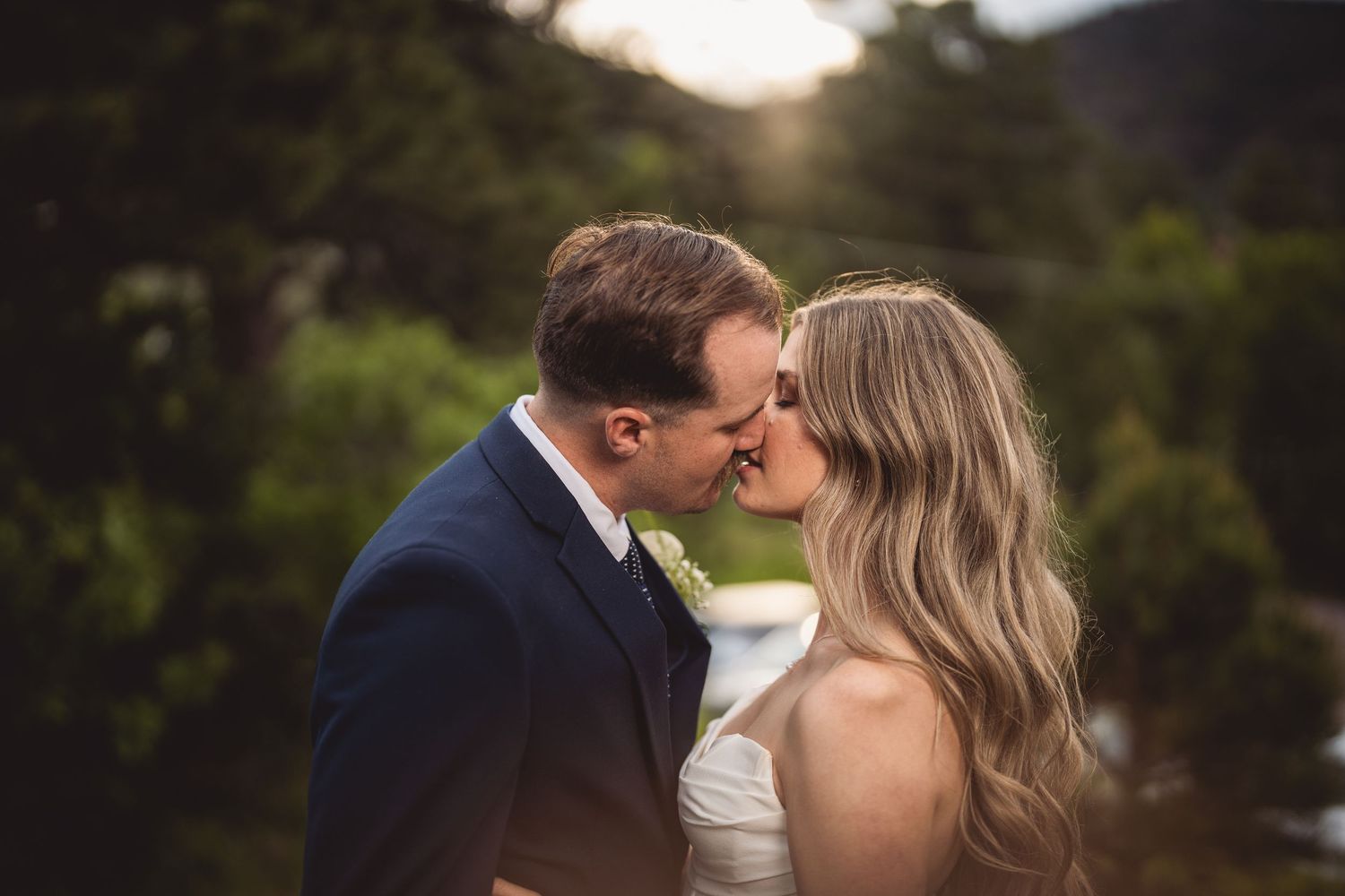 Romantic outdoor wedding photo against a mountain landscape at golden hour.