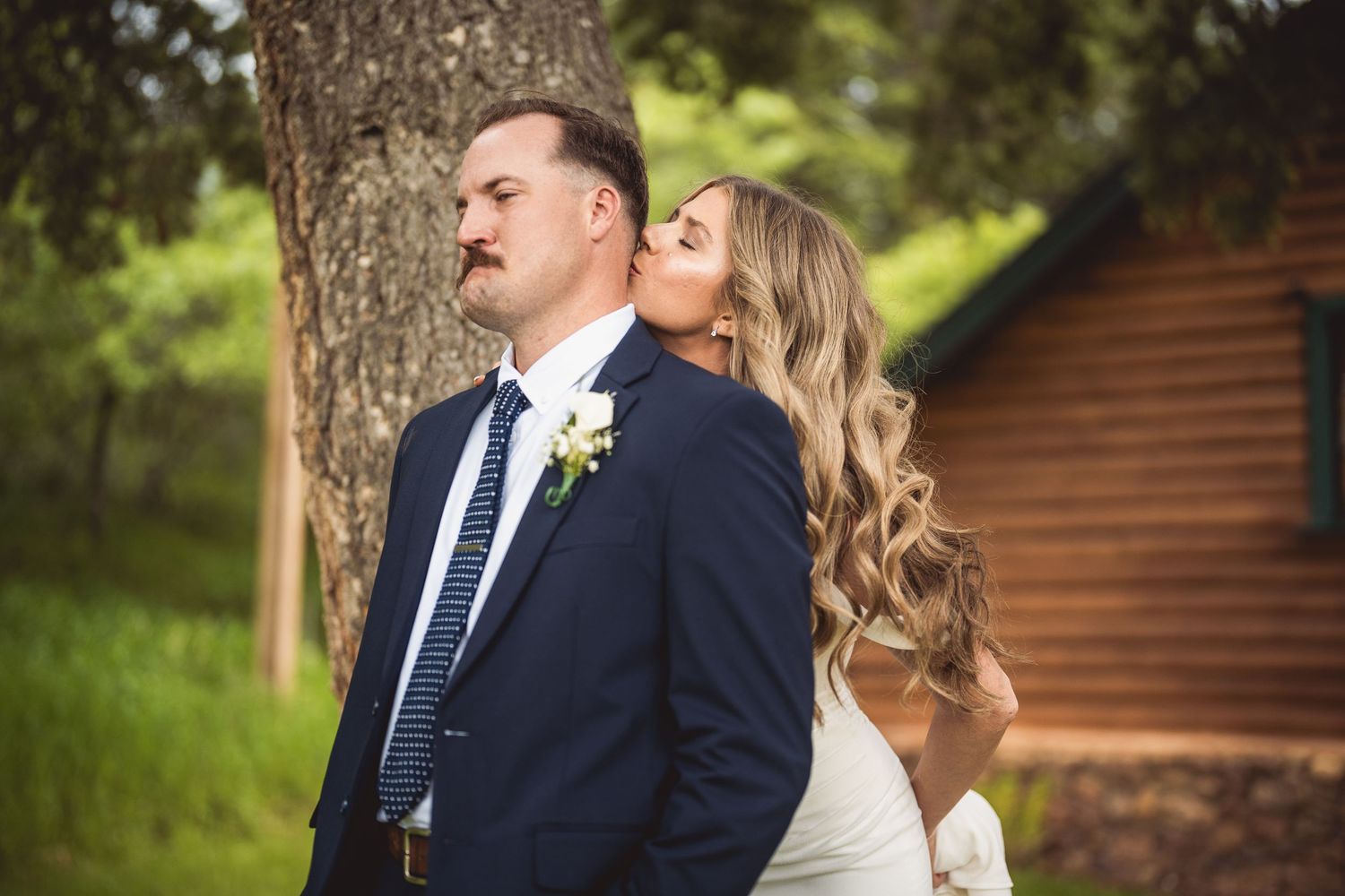 Wedding couple portraits taken in natural outdoor setting with rustic cabin in background.