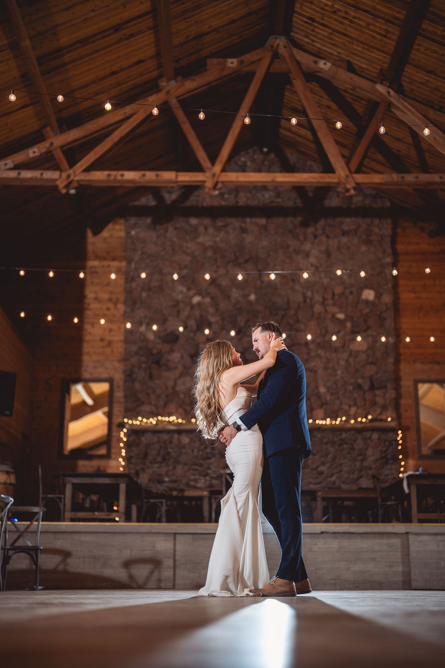 Dancing couple twirls gracefully across wooden floor in rustic barn with string lights overhead.