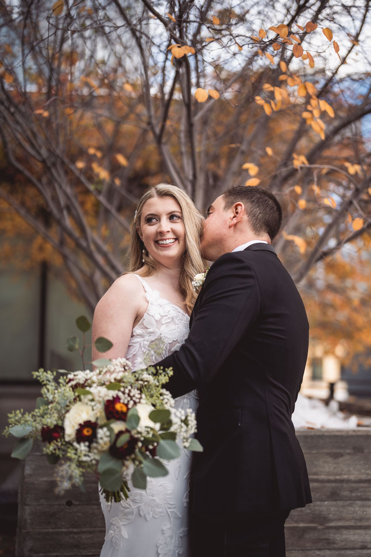 Autumn wedding portrait of couple with fall foliage and white floral bouquet.