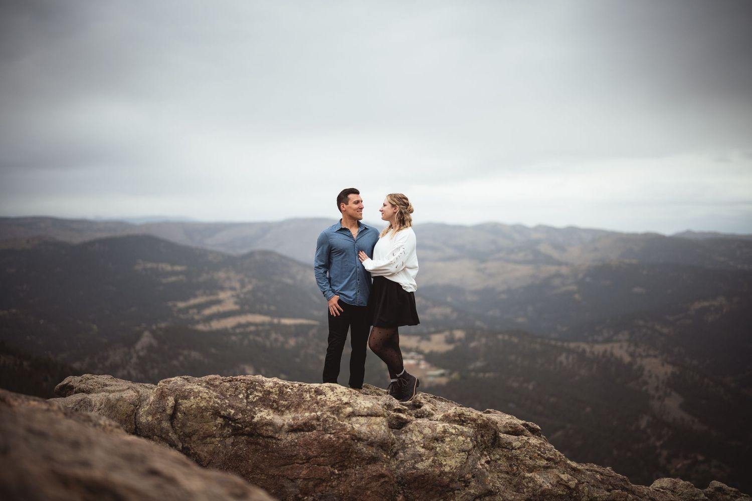A couple enjoys a scenic mountain view while sitting on a rocky overlook.