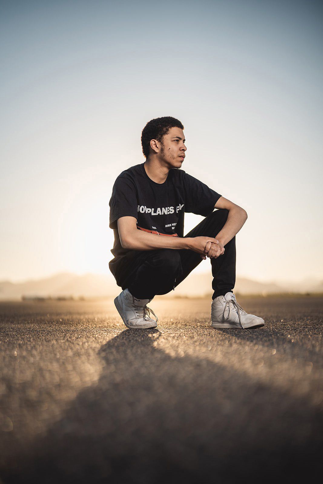 Low angle shot of figure crouching on gravel at sunset wearing black clothing.