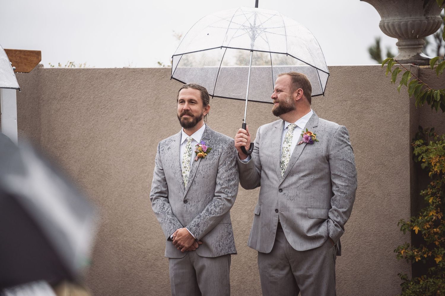 Groomsmen in grey suits sharing a moment before wedding ceremony.