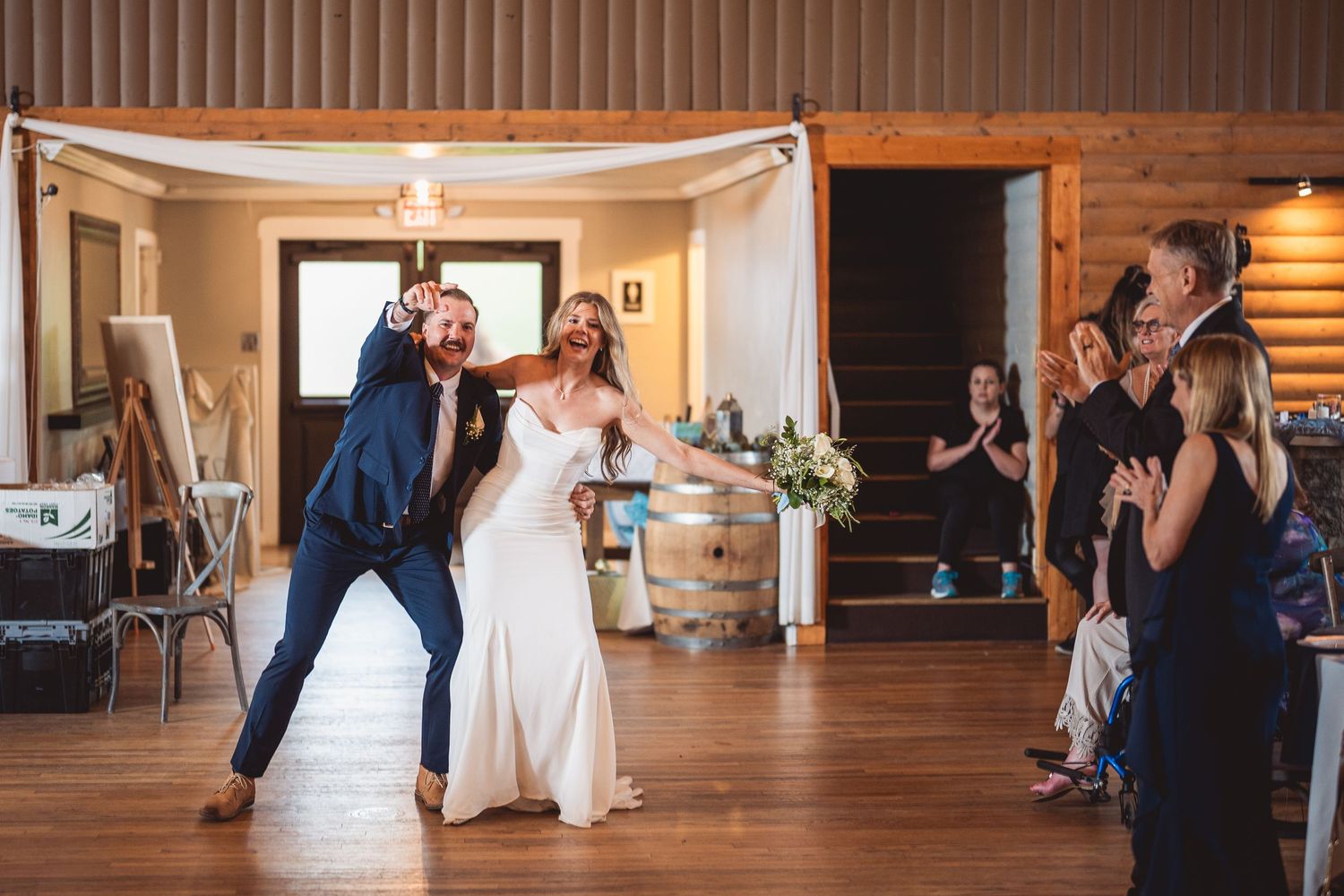 Wedding reception in a rustic wooden venue with guests dancing and celebrating.