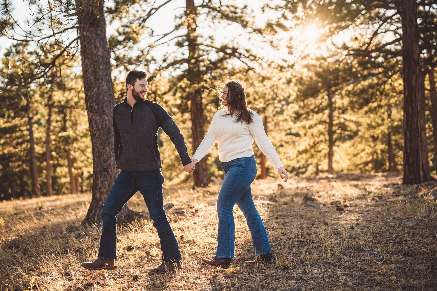Two people dance playfully together in a sunlit mountain forest setting.