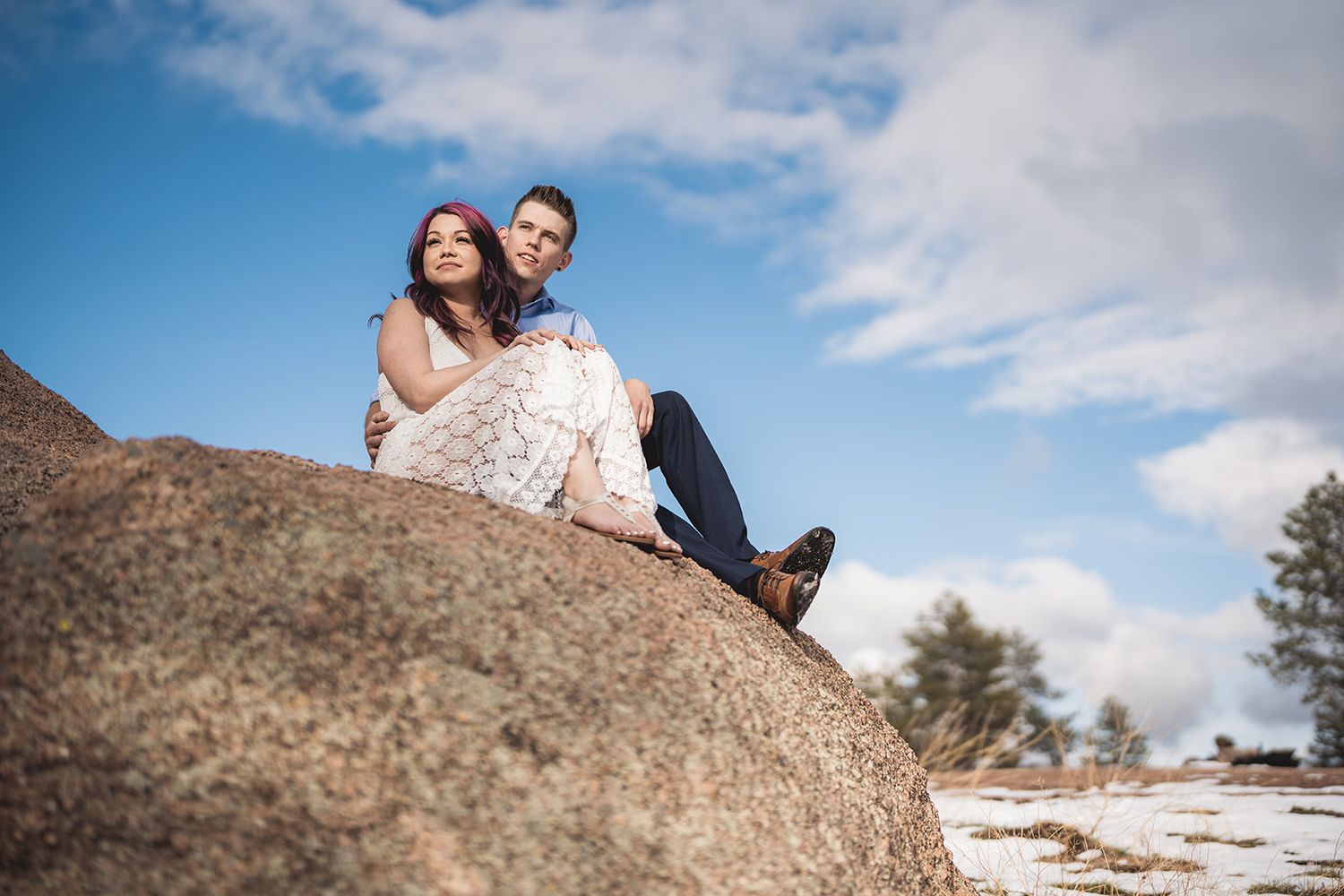 Couple sharing tender moments while sitting on large boulder formations under blue skies.