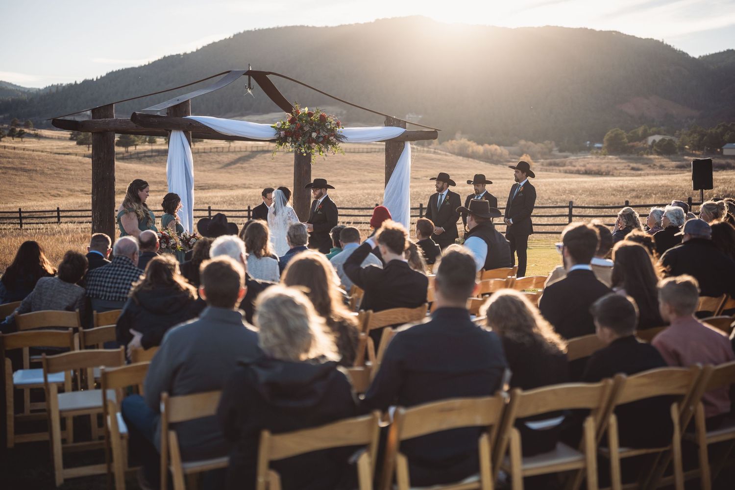 Panoramic view of wedding ceremony setup with wooden benches against mountain backdrop at sunset.
