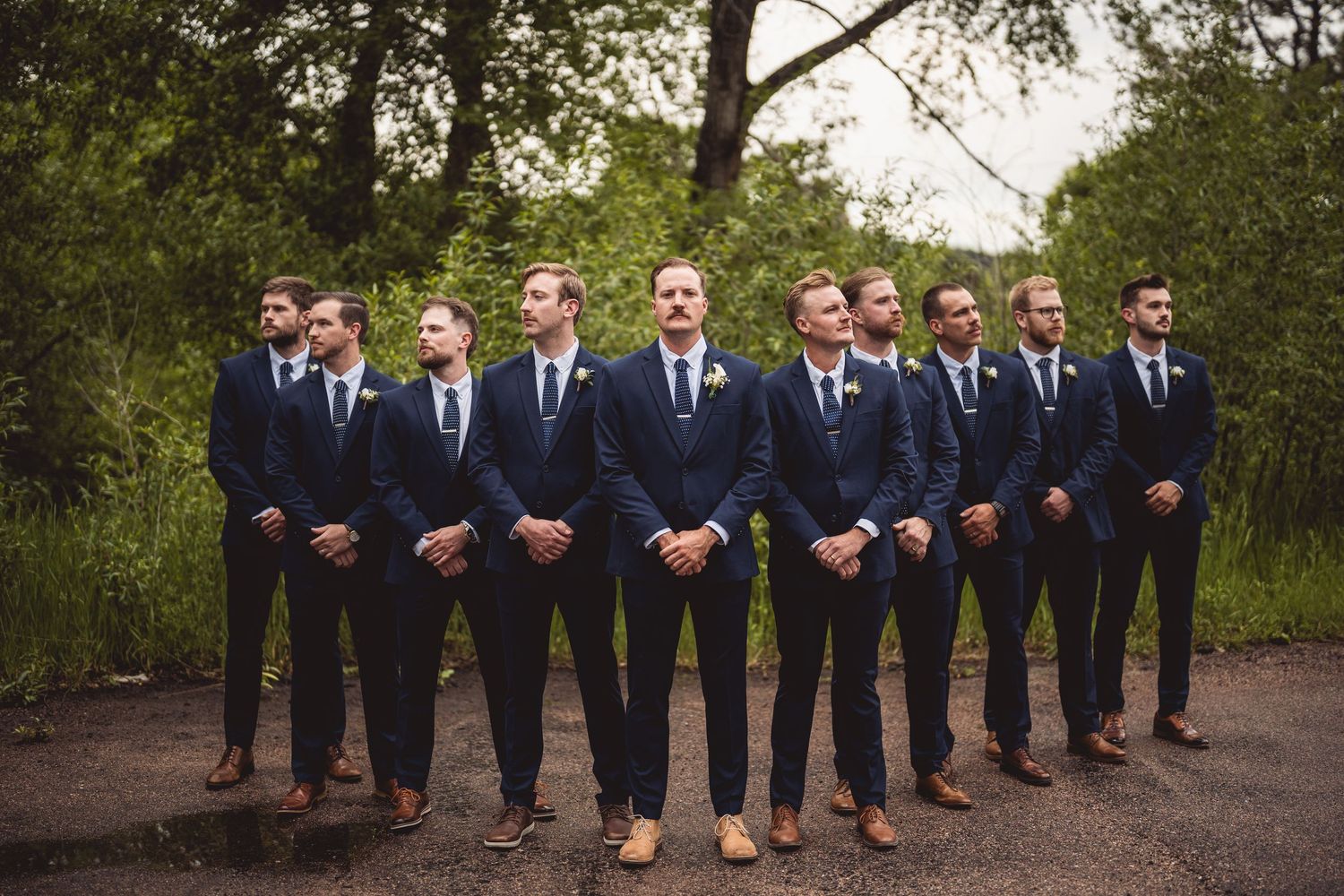 Groomsmen in navy suits and brown shoes lined up for a formal group photo.