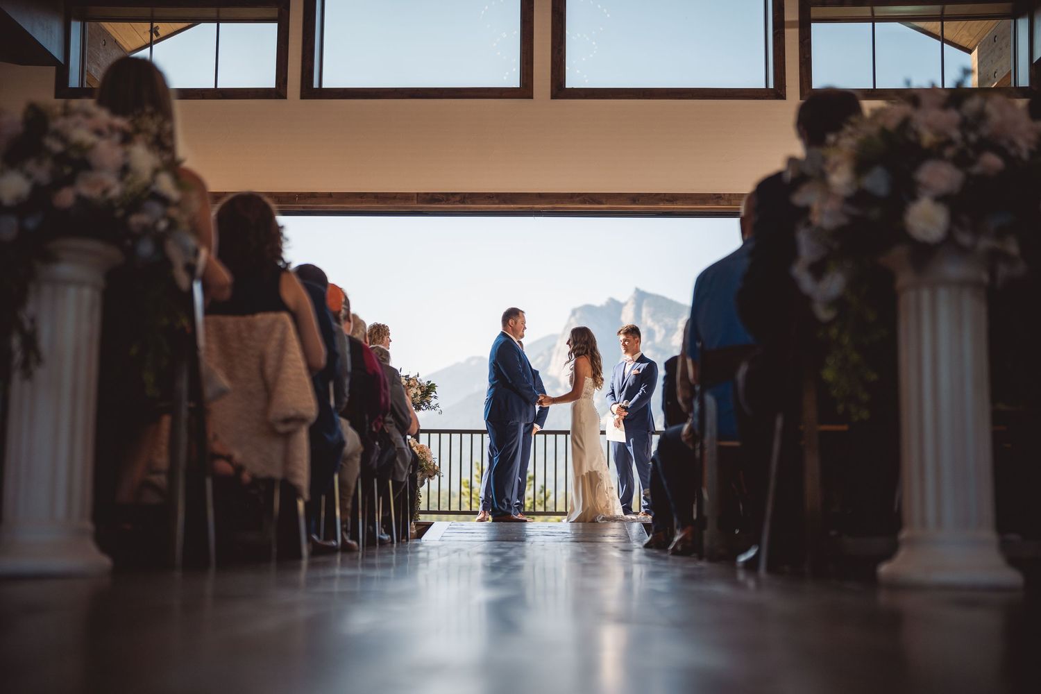 Couple exchanges vows at elegant mountain wedding ceremony with floral columns and panoramic views.