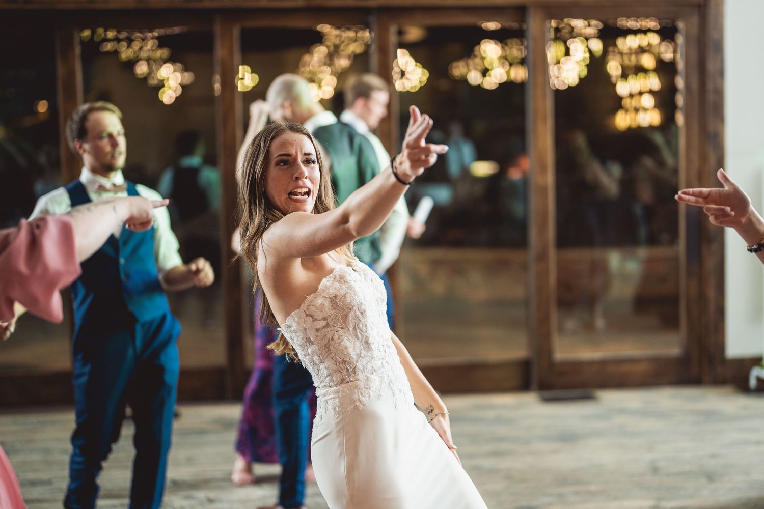 Bride in lace wedding gown tossing bouquet on dance floor at elegant rustic wedding reception.