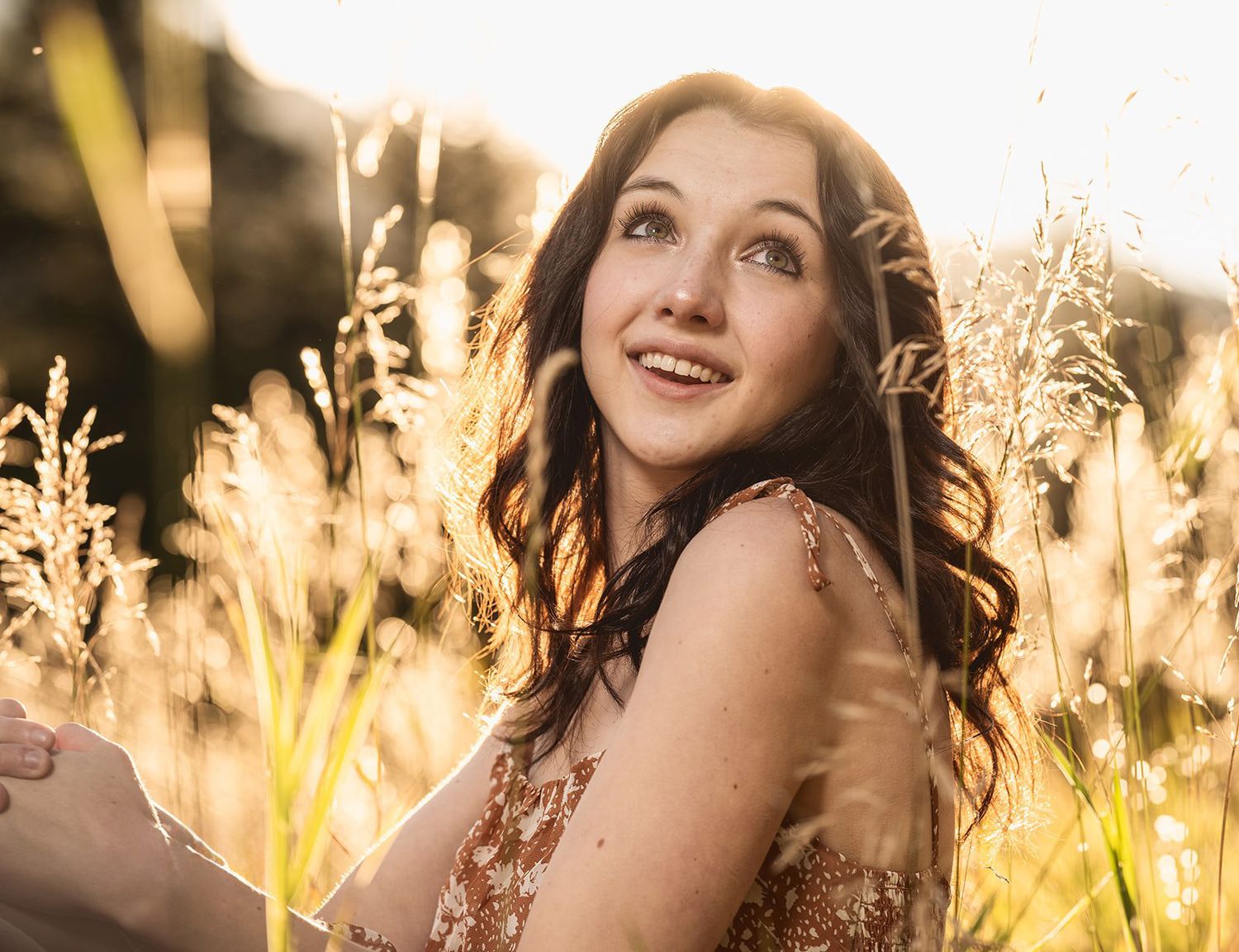 Young woman with dark hair smiling upward in golden sunlit field with tall grass.