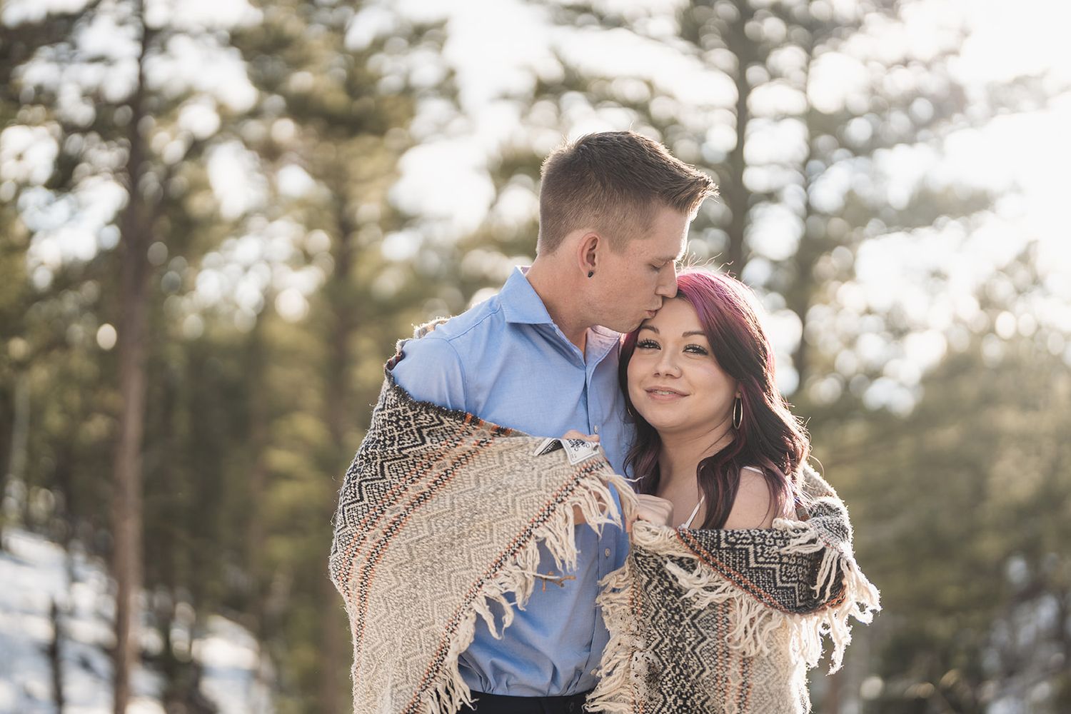 Romantic couple standing in scenic mountain forest with pine trees during golden hour light.