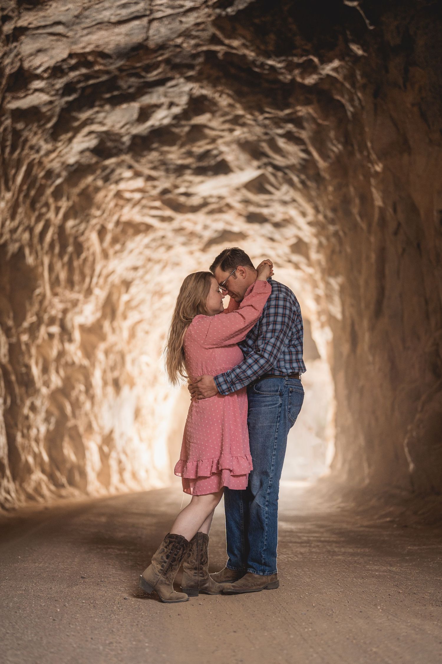 Intimate moment captured in warm-lit cave tunnel with textured rock walls.