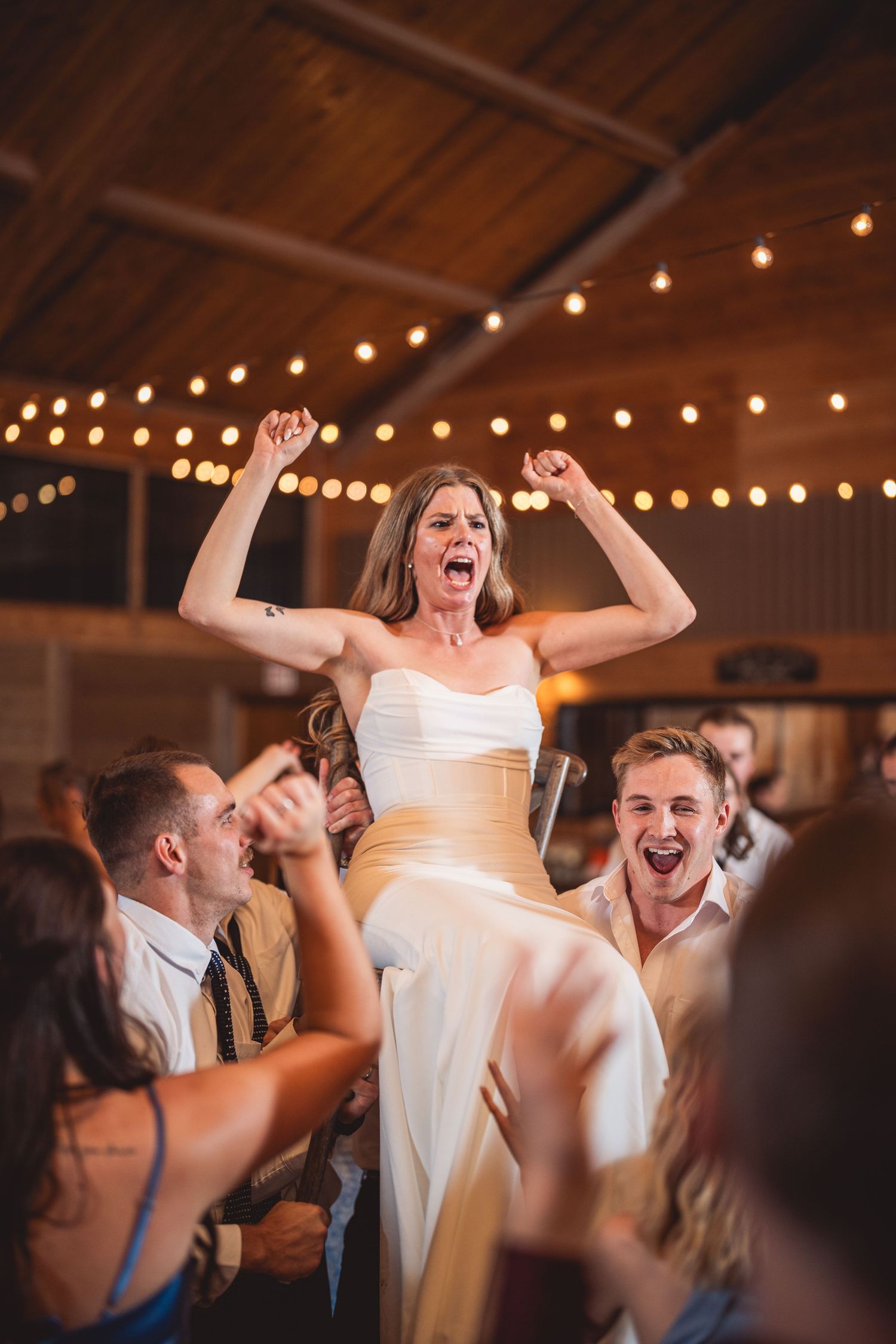 Wedding celebration with energetic dancing and celebration under string lights in rustic venue.