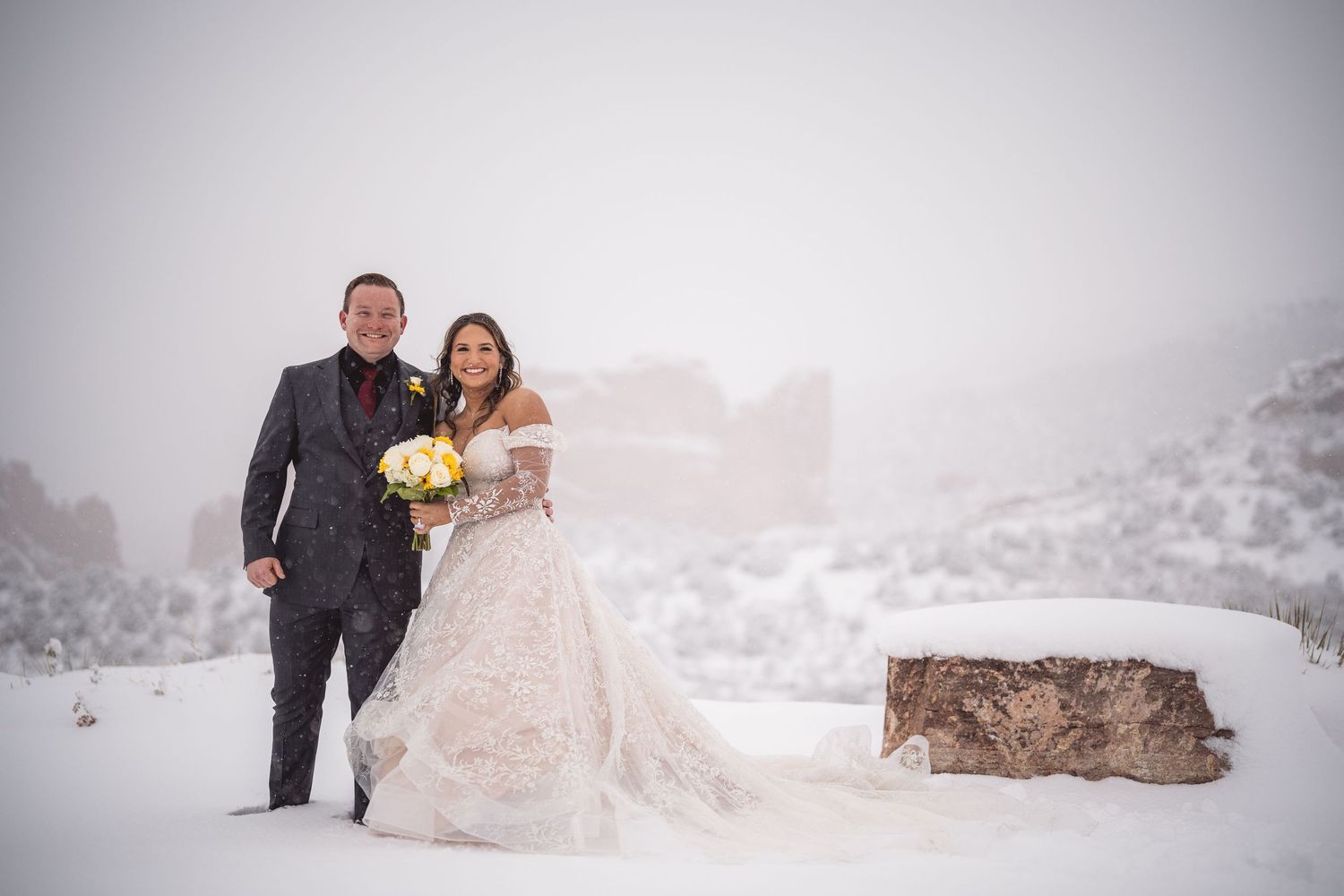 Winter wedding couple poses in snowy mountain landscape wearing formal attire.