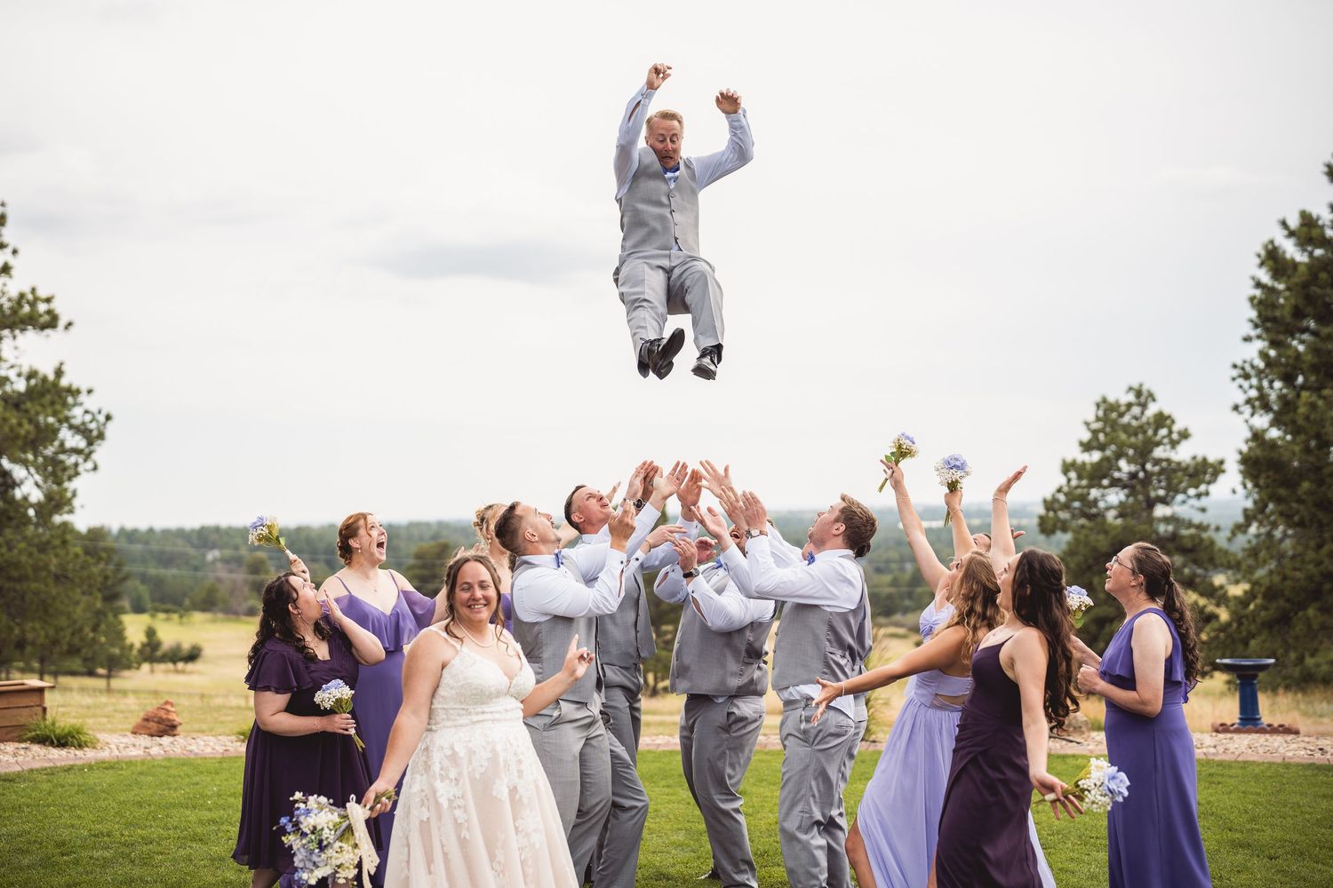 Wedding party celebrating outdoors with jumping poses and purple bridesmaid dresses.