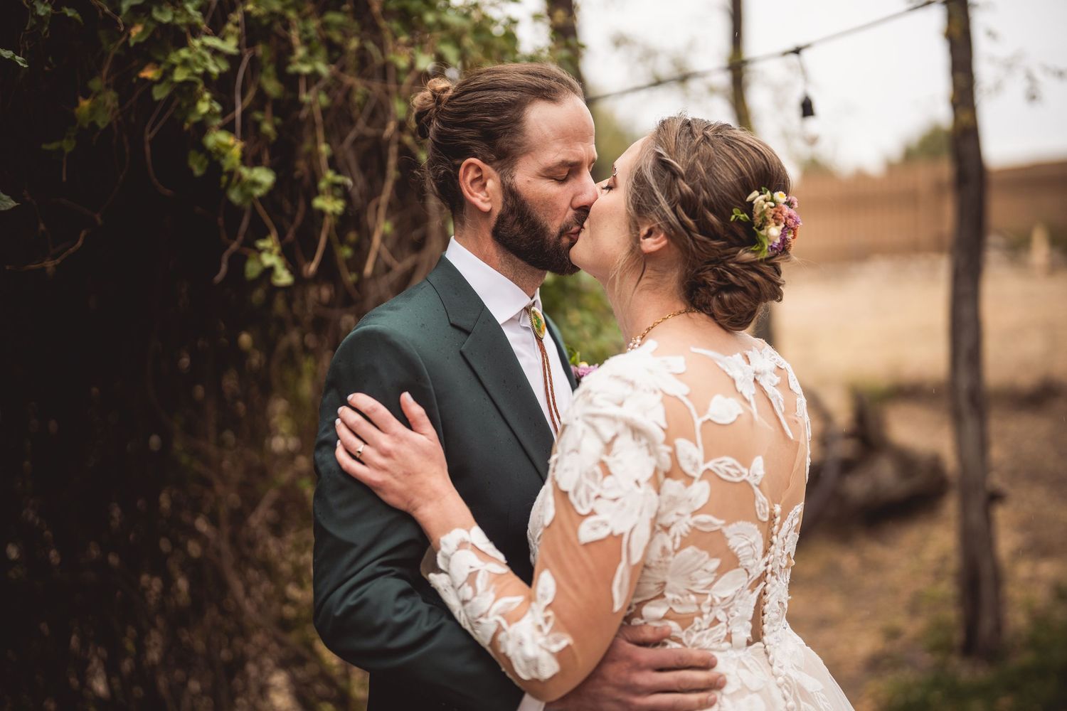 Wedding couple embraces in romantic outdoor setting with natural foliage backdrop.