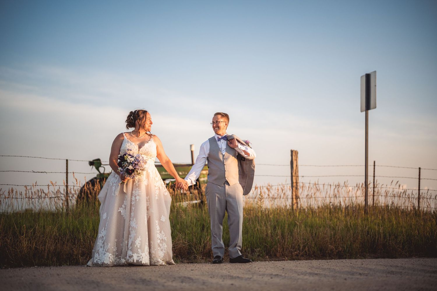 Wedding couple silhouetted in a panoramic sunset shot with scenic fence and meadow background.
