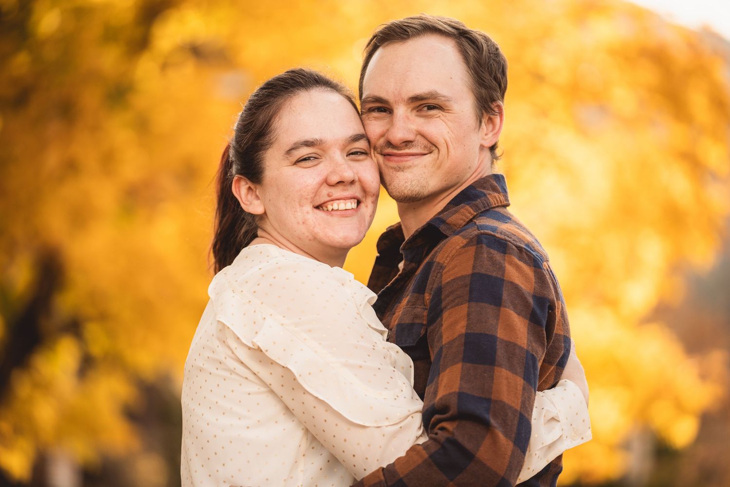 Loving couple embraces while surrounded by vibrant yellow autumn leaves in an outdoor setting.