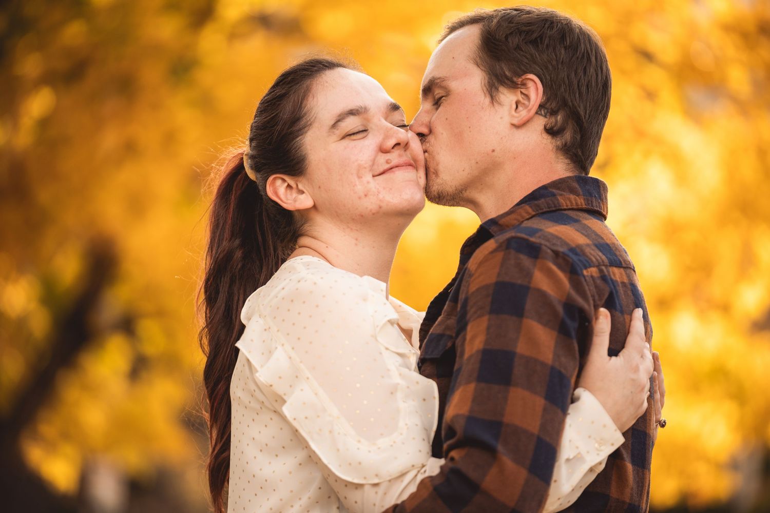 Tender moment captured between couple against glowing autumn foliage background.