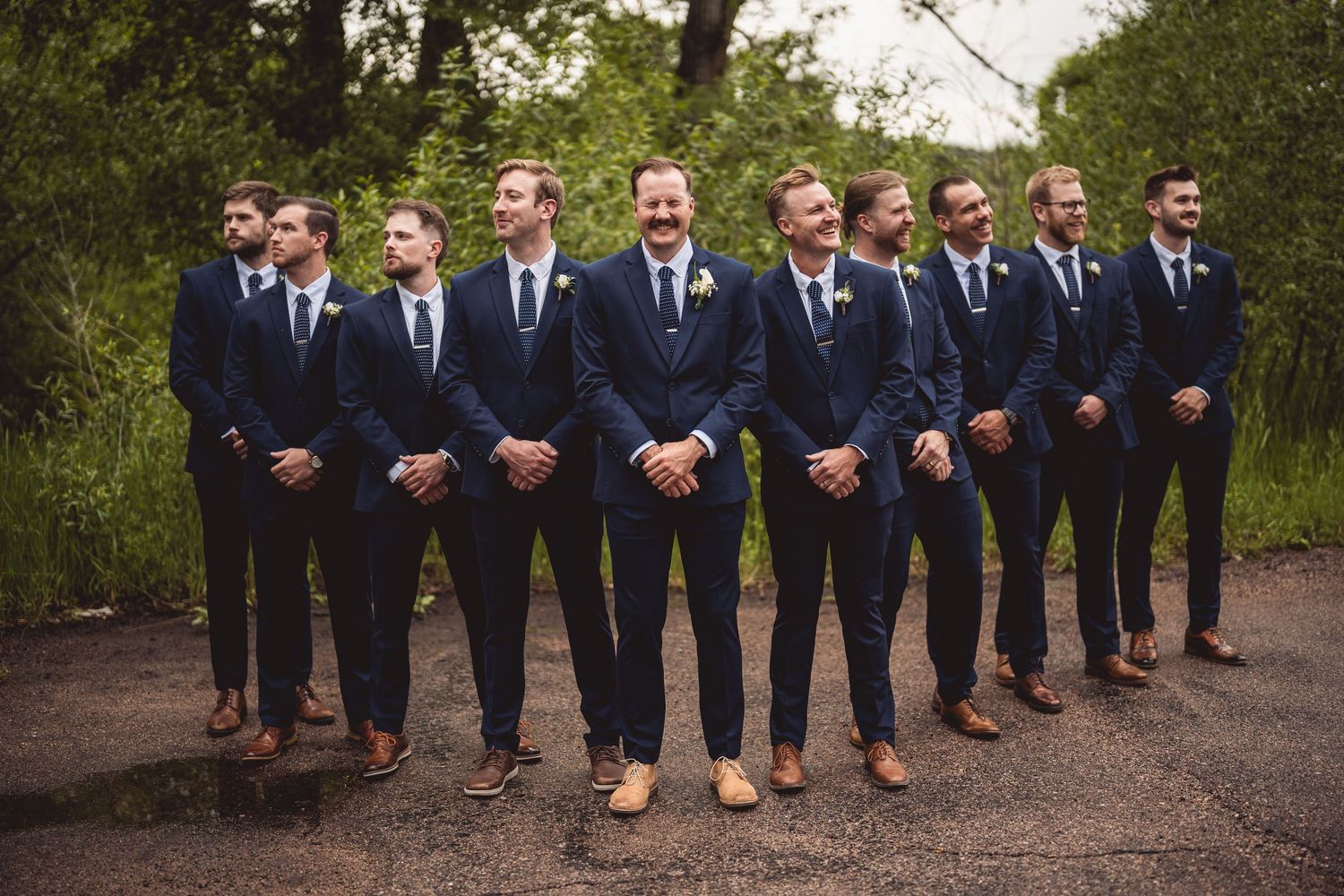 Wedding party of groomsmen in matching navy suits posing outdoors.