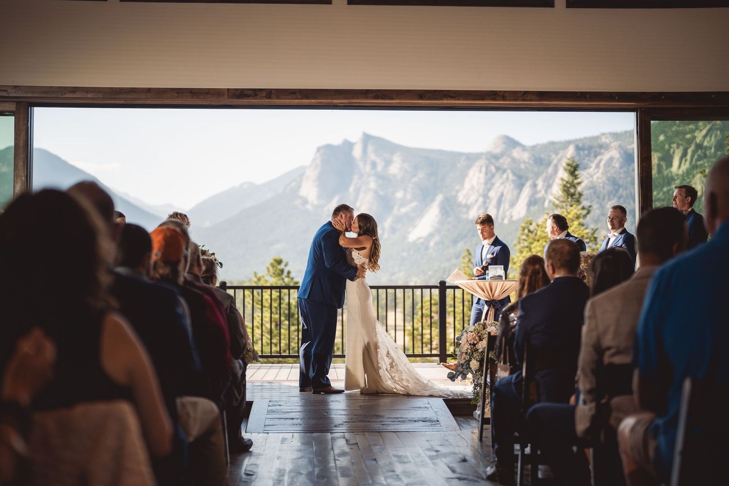 Bride and groom share first kiss at stunning mountain backdrop wedding ceremony with seated guests.