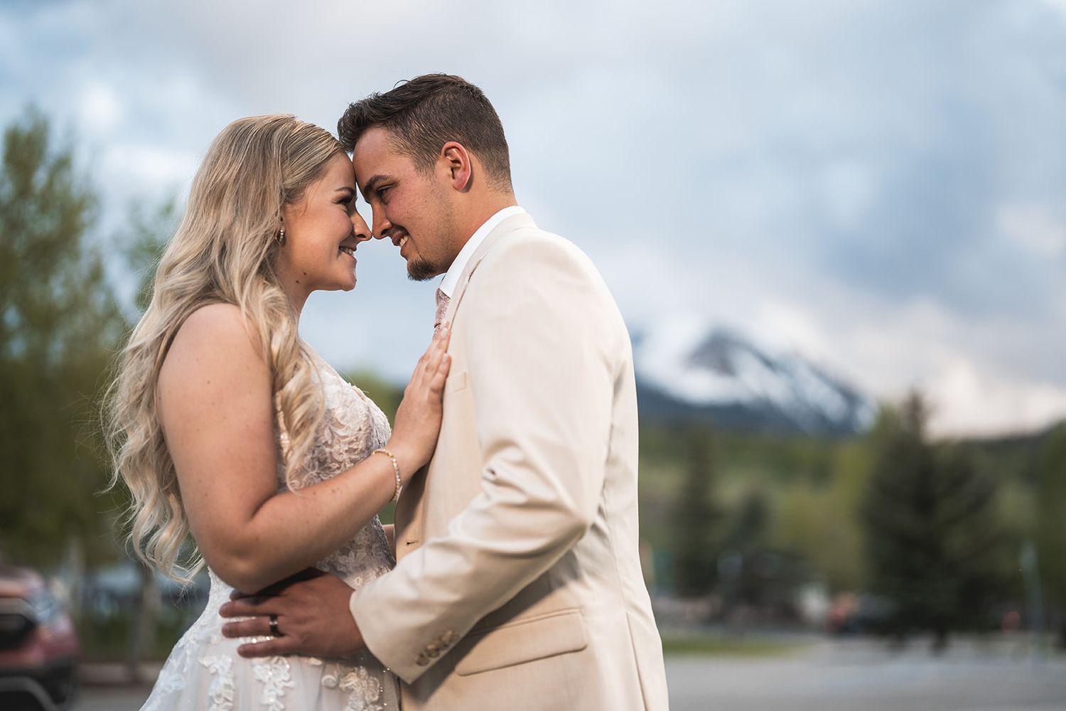 Bride and groom share a romantic moment outdoors with snow-capped mountains in the background.