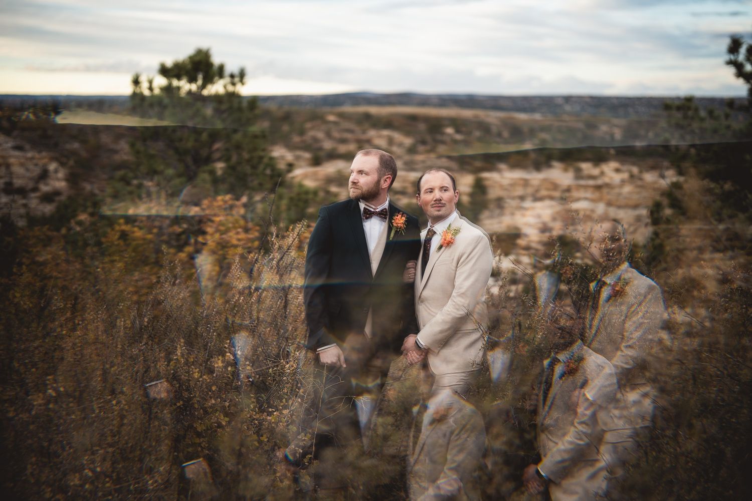 Two grooms holding hands outdoors at a scenic canyon wedding venue in natural surroundings.