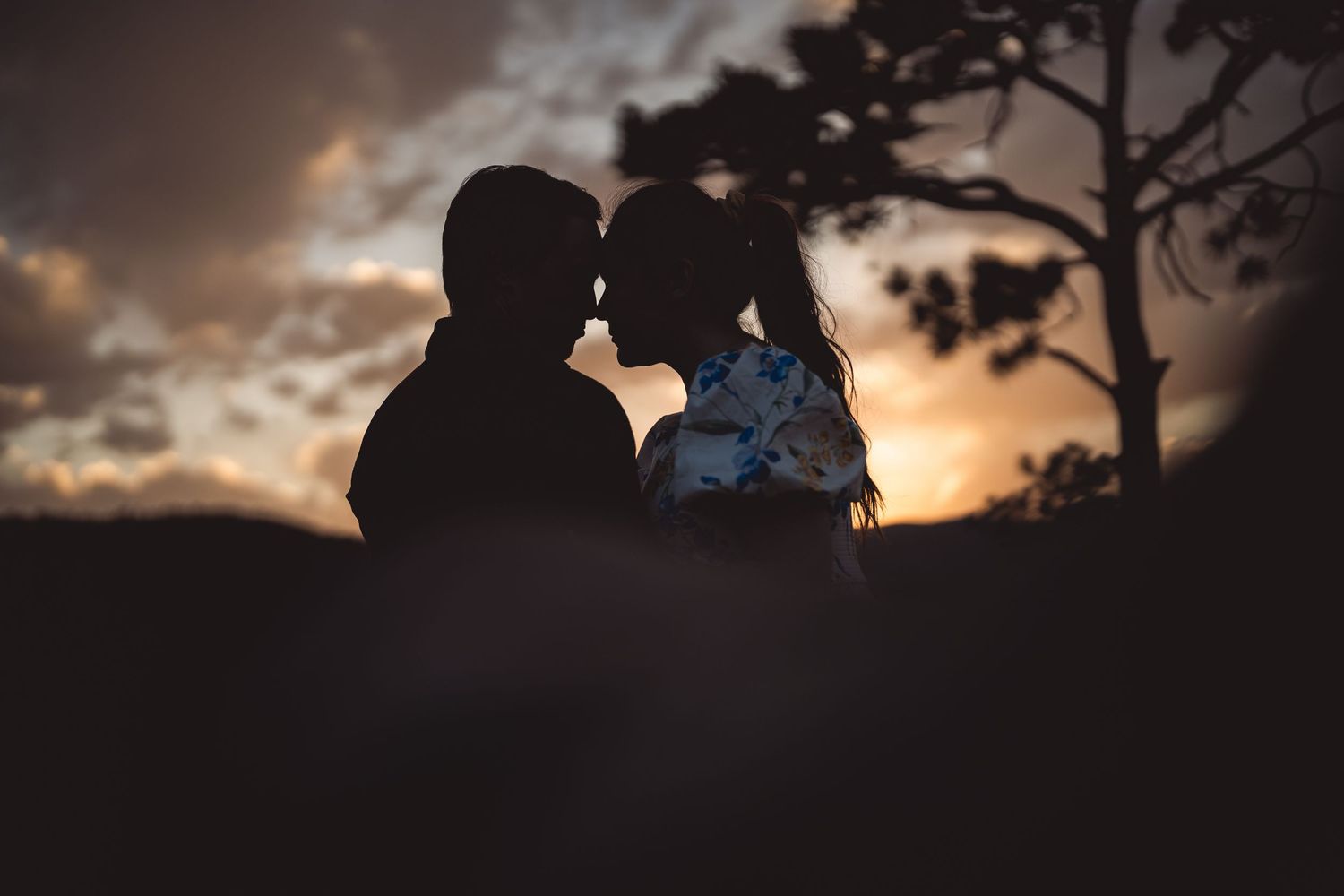 Romantic couple silhouette sharing a tender moment against a stunning golden sunset sky.